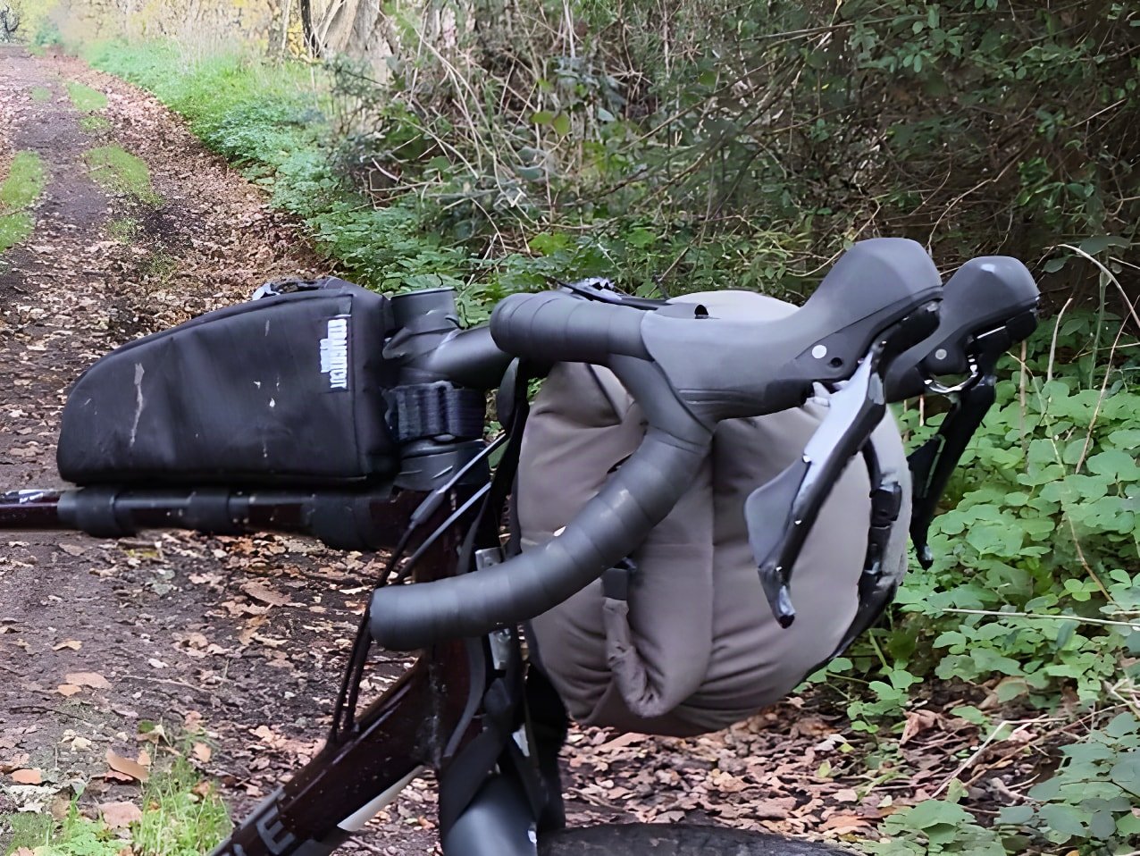 Straight Cut Design handlebar harness holding a dry bag on a drop-bar gravel bike on a woodland track.