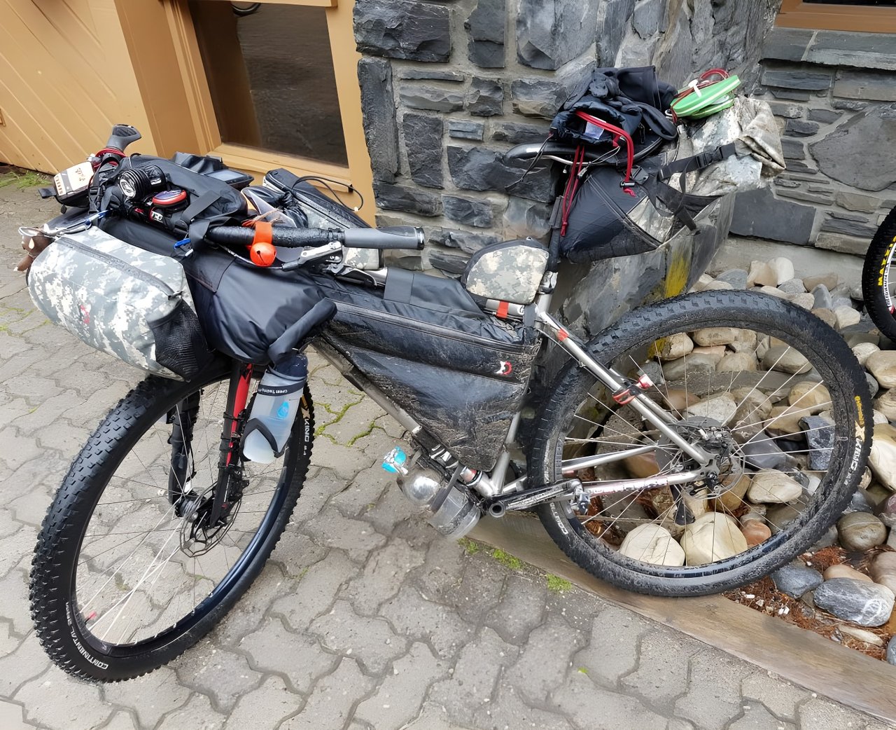 Tour Divide bikepacking bike loaded with frame, bar and seat bags, parked on paving against a stone wall.