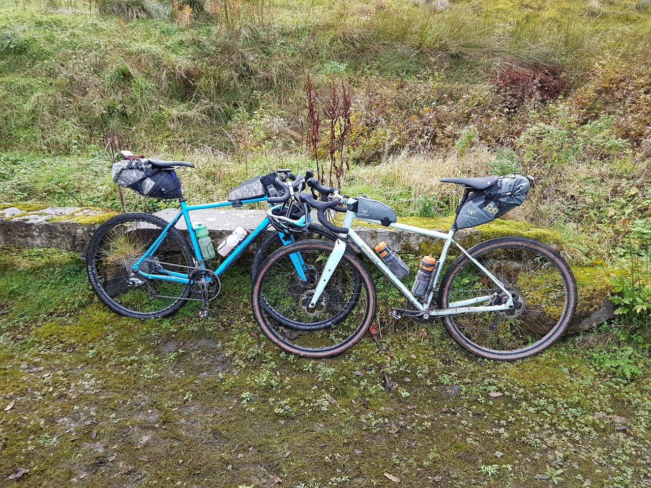 Two gravel bikes with drop bars and bikepacking bags leaning against a mossy stone wall.
