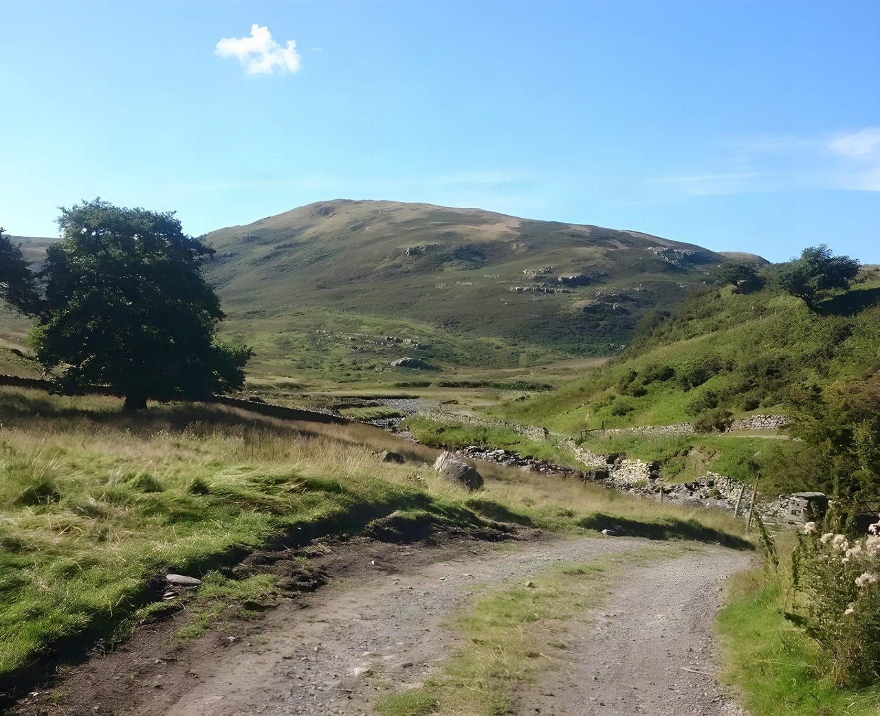Stony track climbing through a green valley beneath a rounded fell, on the Chasing Trails MTB Coast to Coast.