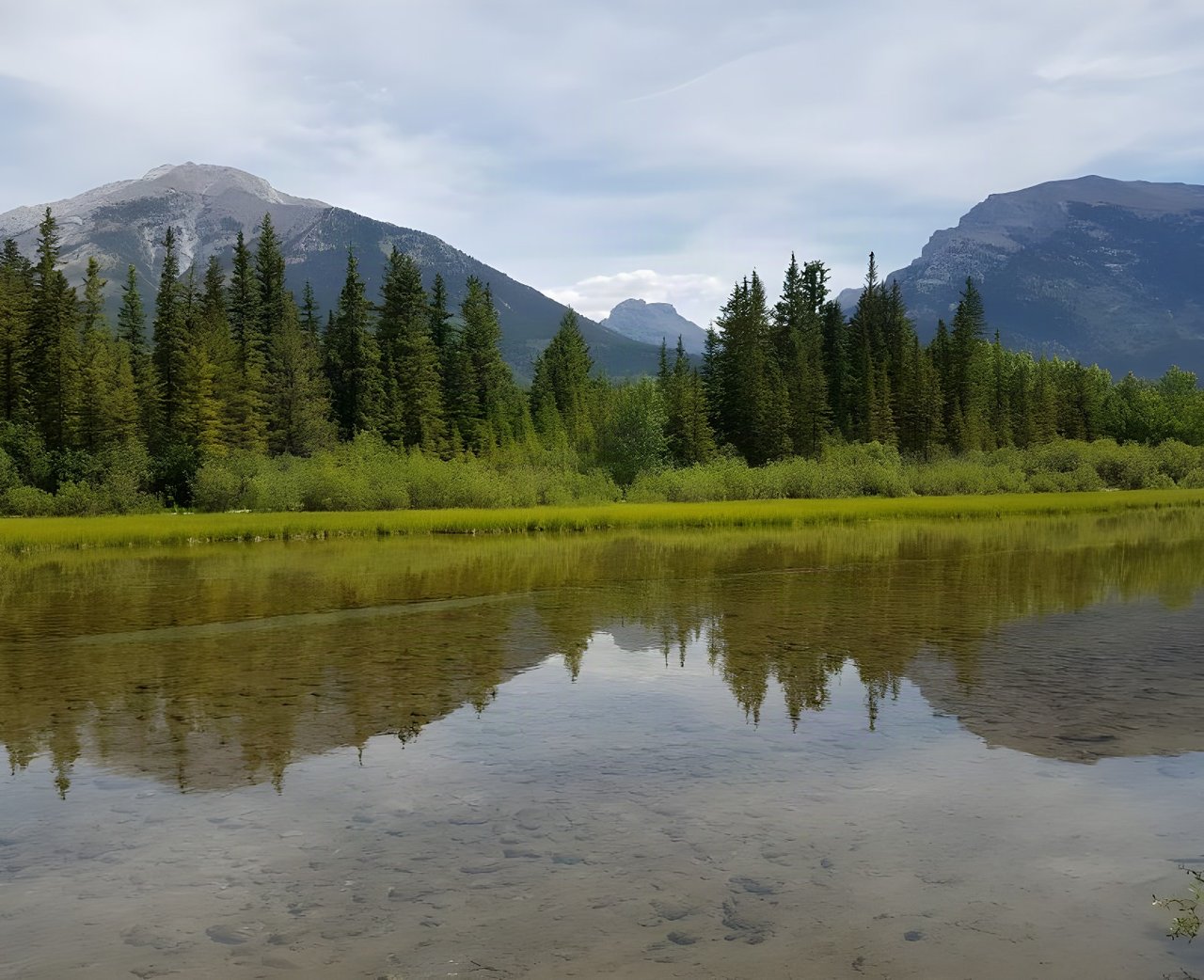 Calm lake reflecting conifers below bare mountain peaks, the kind of scenery the Tour Divide rides through.