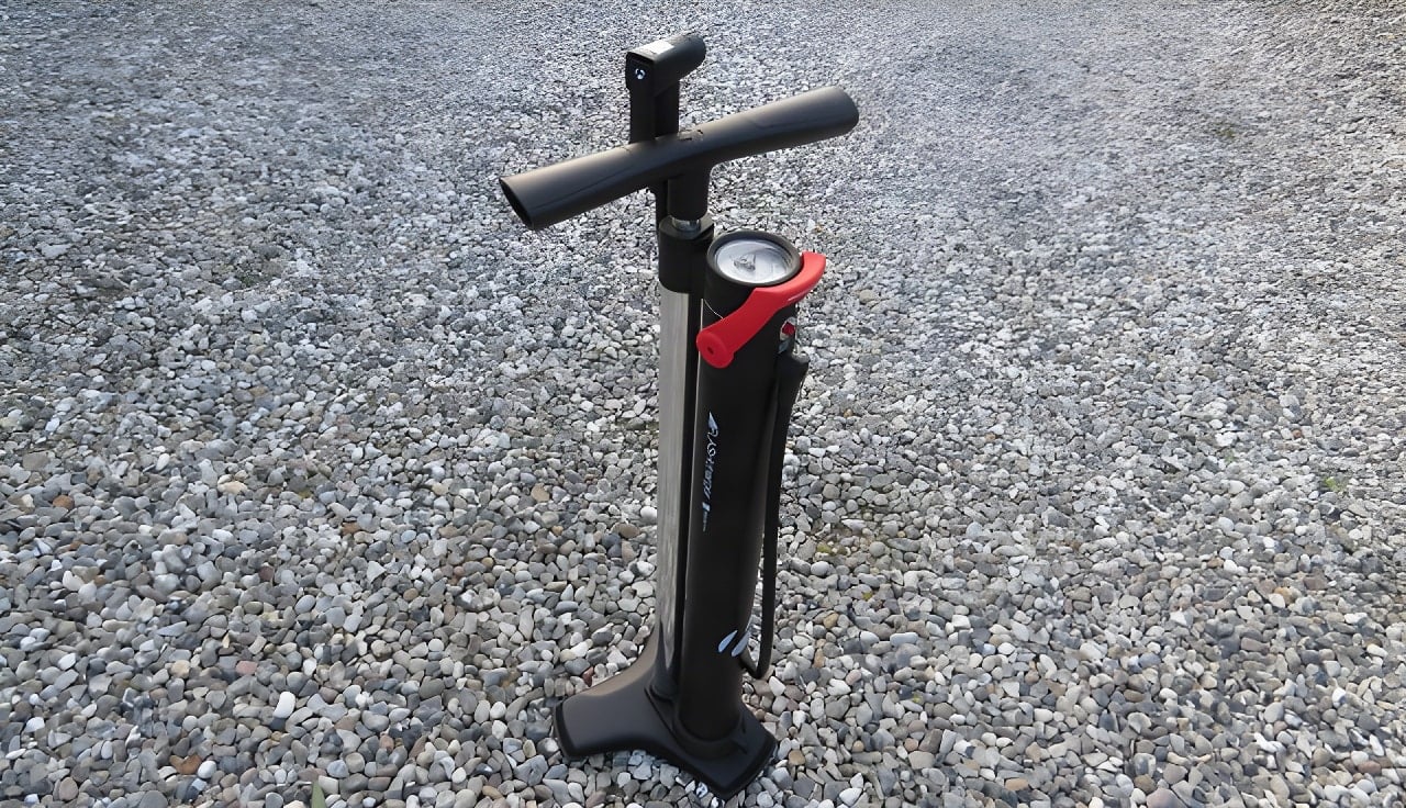 Bontrager Flash Charger tubeless track pump standing on gravel, with red charge lever and pressure gauge.