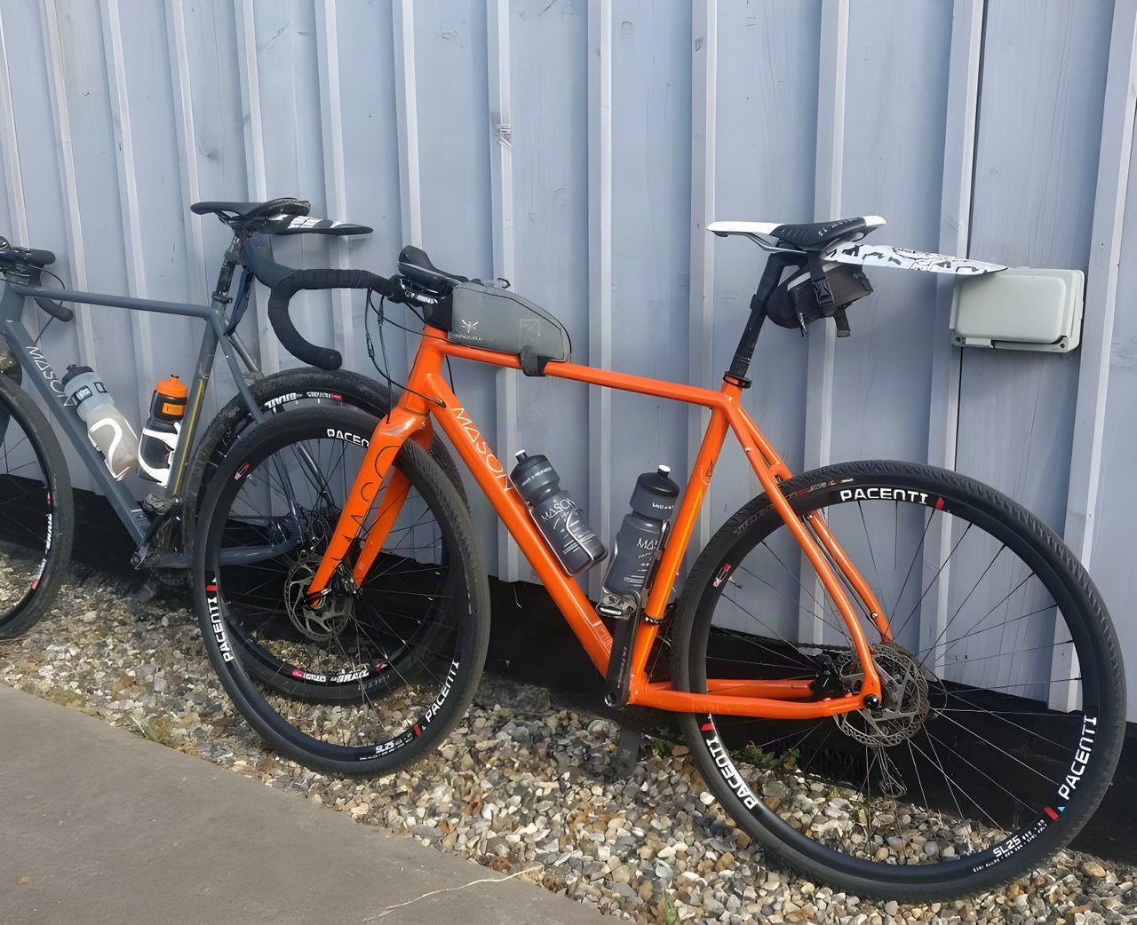 Two Mason Bokeh bikes, one orange and one grey, leaning on a metal-clad wall at the Suffolk Byways Audax.