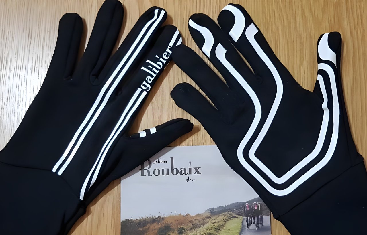 Pair of black Galibier Roubaix Vision gloves with white stripes lying on a wooden table beside a Roubaix glove leaflet.