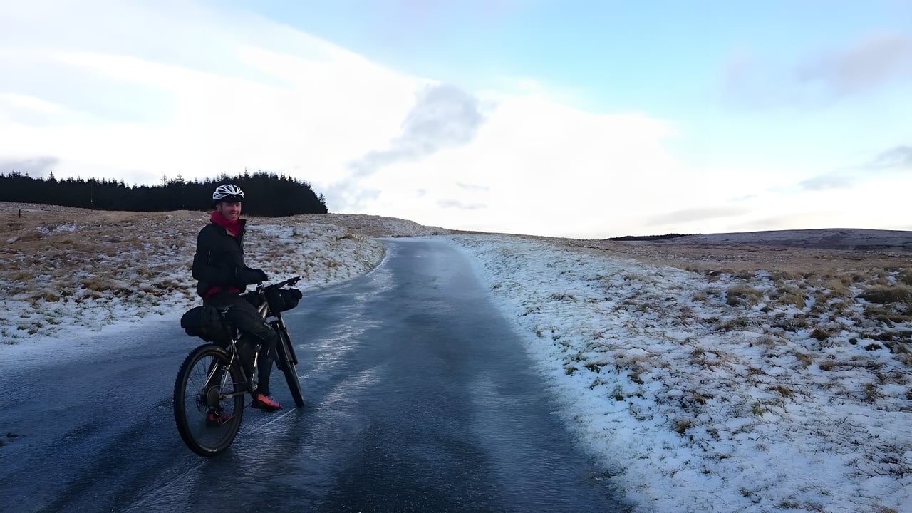 Bikepacker pauses on an icy road climbing towards Llangurig, snow on the moorland, for the Cafe Racer winter event.