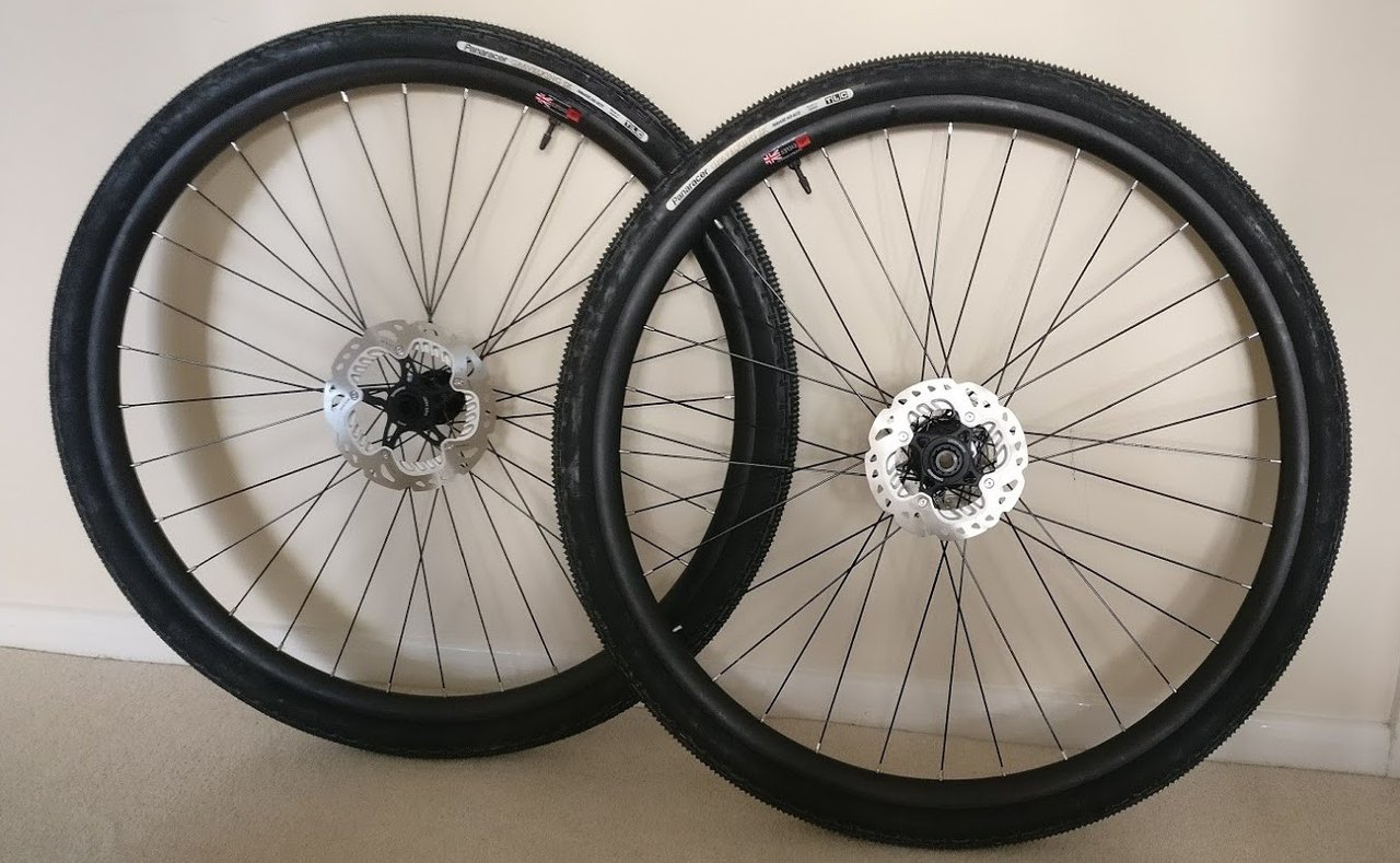 Homebrew carbon gravel wheelset with Panaracer GravelKing SK tyres and Shimano disc rotors, leaning against a wall.