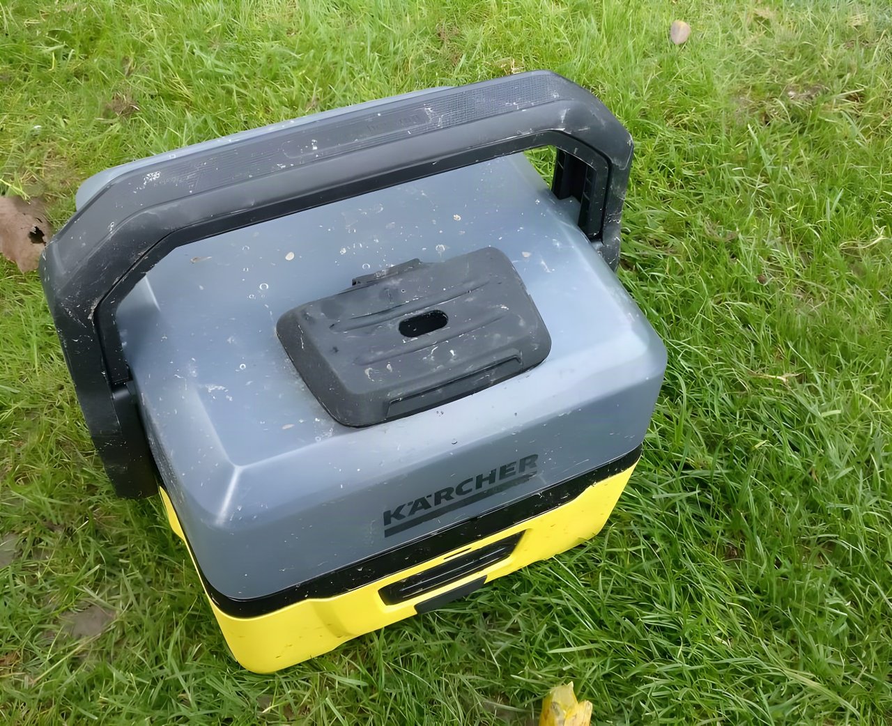 Kärcher OC3 portable washer with grey water container and yellow base standing on grass.