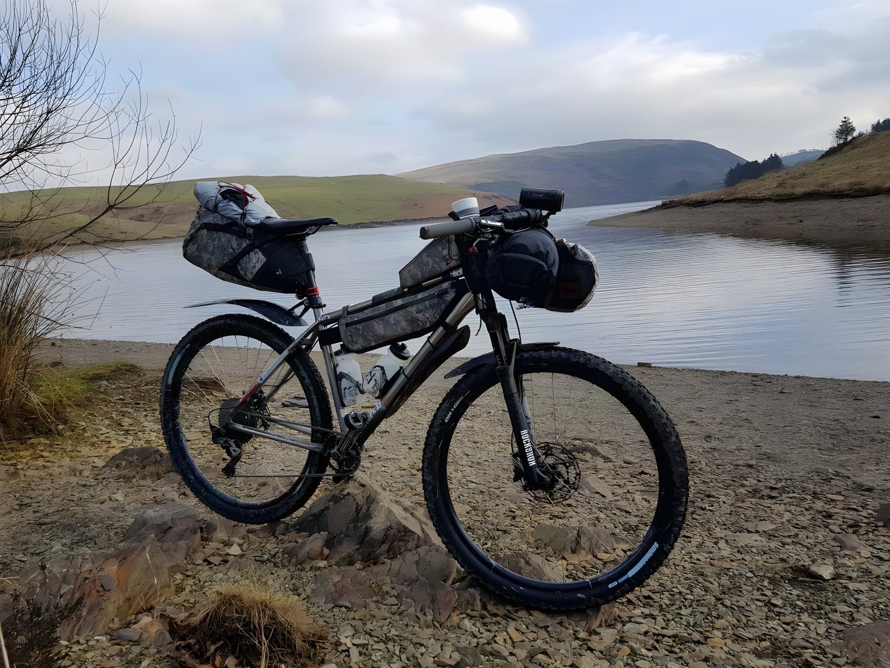 Loaded bikepacking hardtail with frame, bar and seat bags on the shore of Llyn Clywedog reservoir in mid Wales.