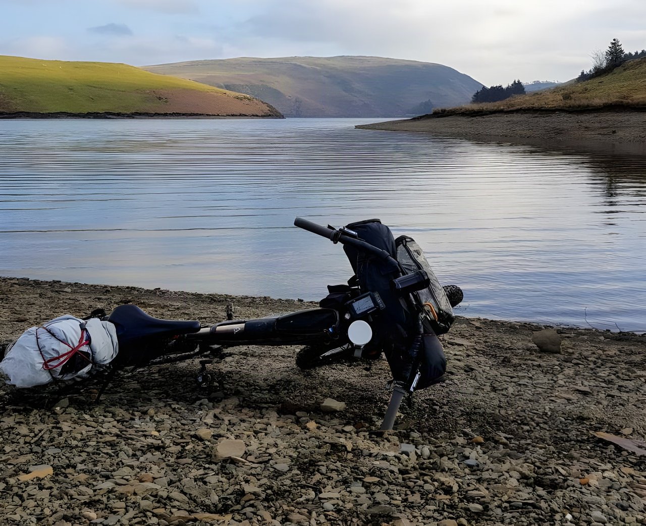 Loaded bikepacking bike lying on the shingle shore of Clywedog Reservoir during the Bearbones Café Racer ride in Mid-Wales.