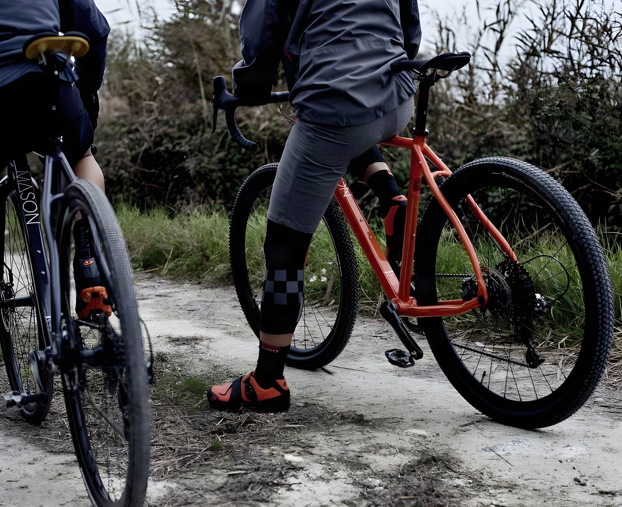 Two riders pause on a chalky track, one astride an orange Mason Bokeh adventure bike, the other on a dark one.