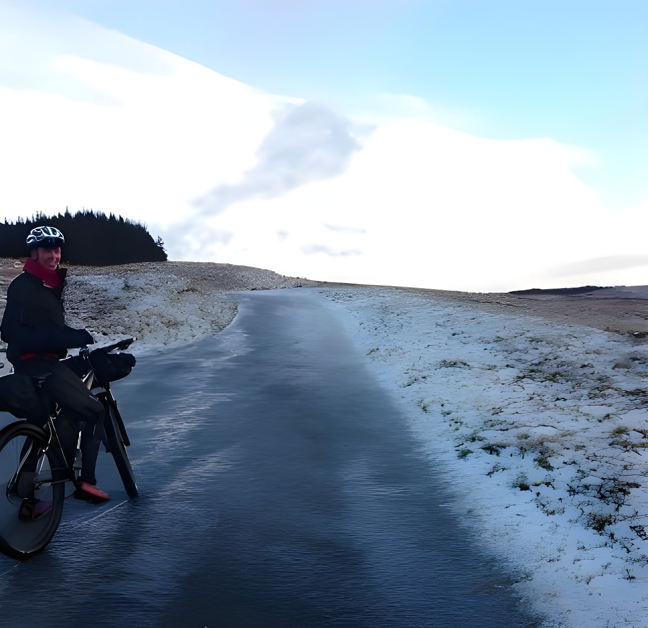 Rider Andy Lawrence with a loaded bikepacking bike on a frosty road beside snow-dusted moorland.
