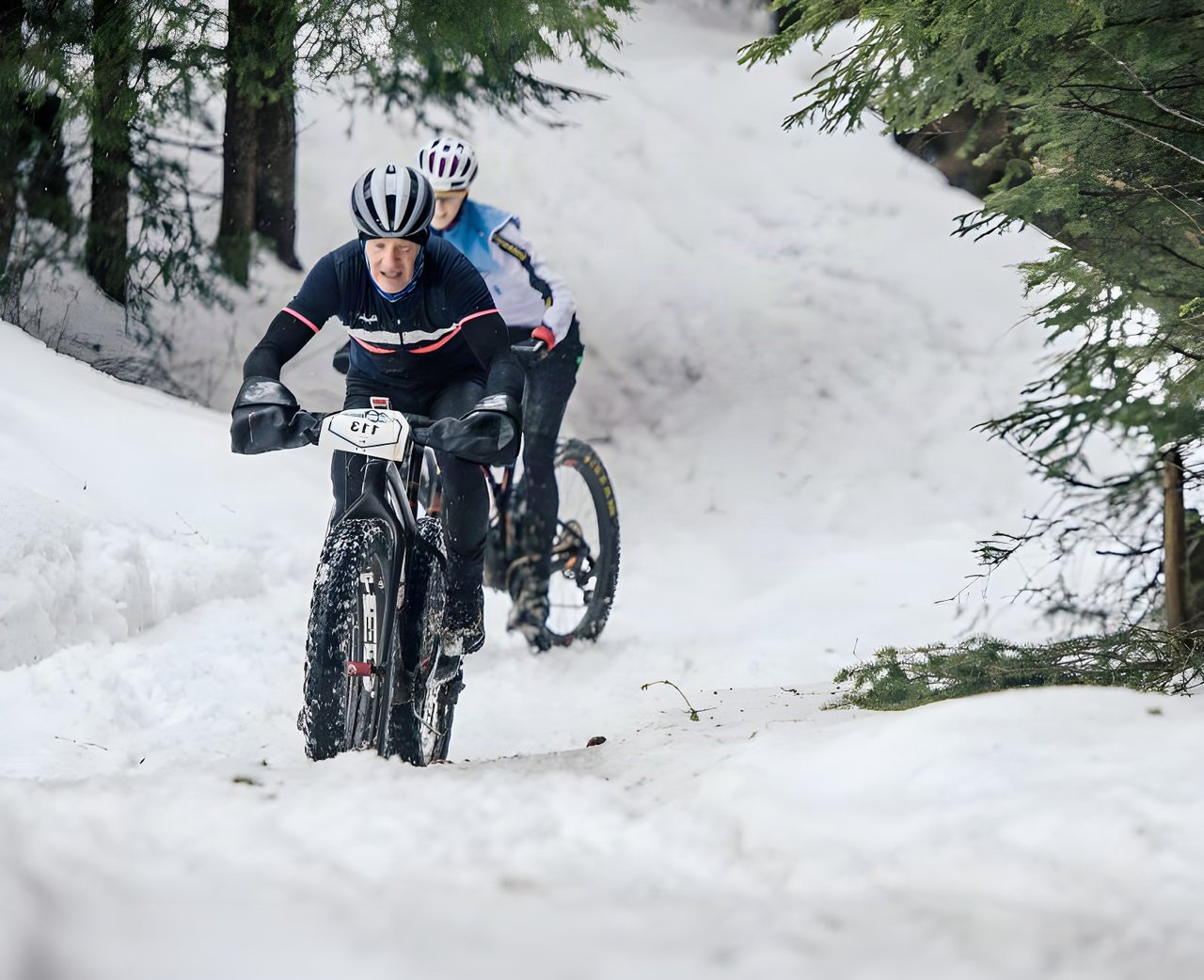 Two fatbike riders descend a snowy forest track on Stage 3 of the Snow Bike Festival in Gstaad.