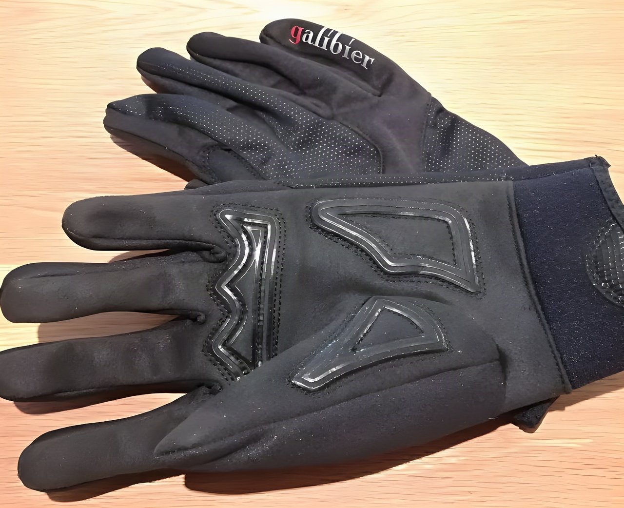 Pair of black Galibier Ardennes winter gloves with silicone grip detailing on the palm, on a wooden table.