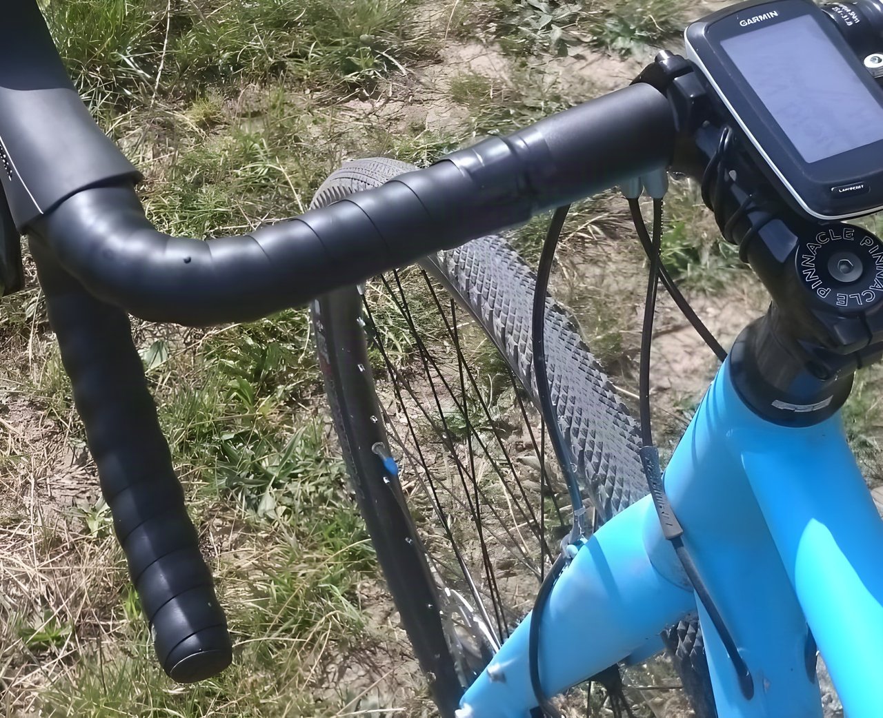 Blue Pinnacle gravel bike's handlebars with a Garmin computer above a fine-tread Specialized Trigger Pro 38c tyre.