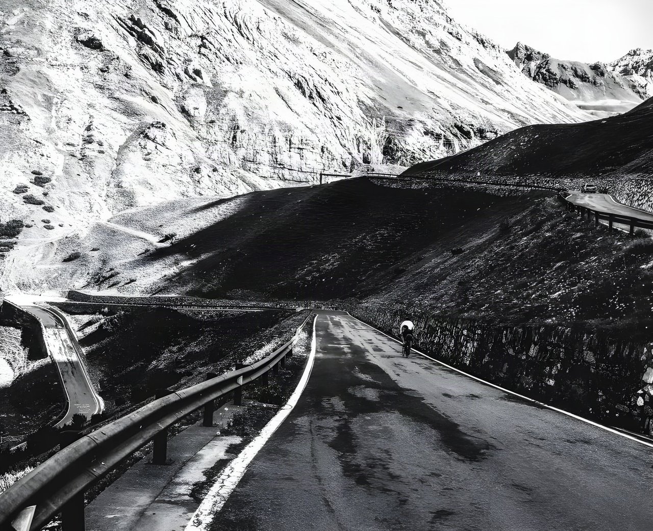 Lone rider climbs a winding Alpine pass road on the Transalp ride from Germany to Italy, in black and white.