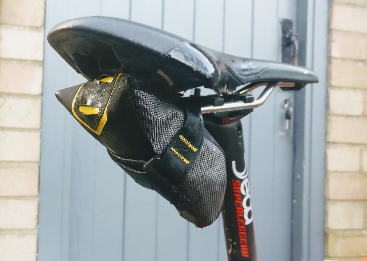Apidura Expedition Tool Pack in dark grey with yellow stitching, Velcro-strapped under a road bike saddle.