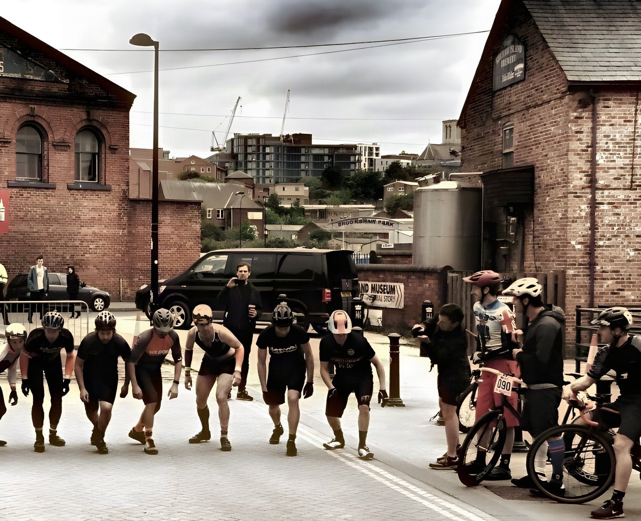 Riders crouch for a running start at the Sheffield Urban Cyclo Cross Kelham Island round, between brick buildings.