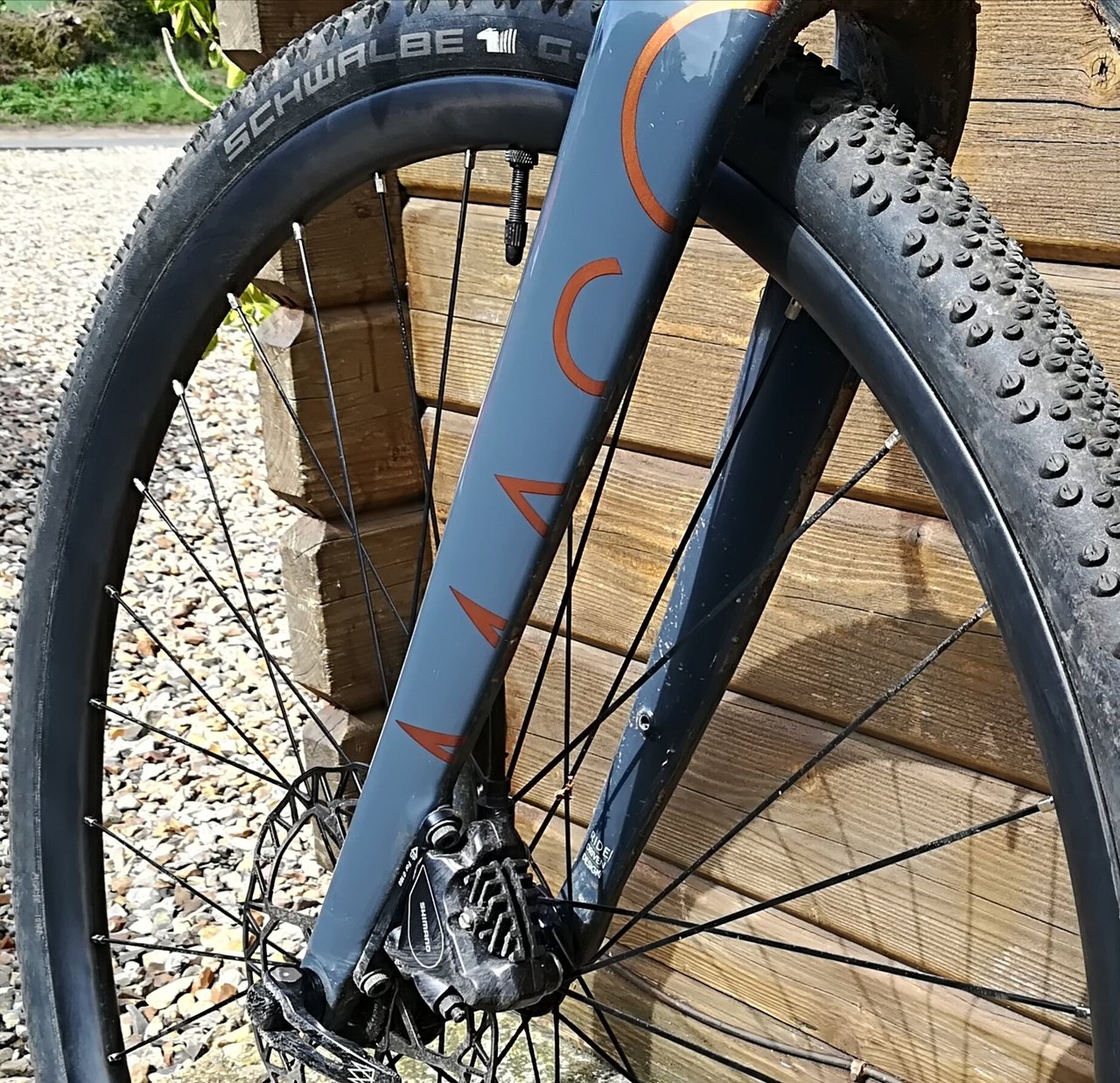A Schwalbe G-One Bite tyre fitted to a grey fork, leaning against wooden crates.