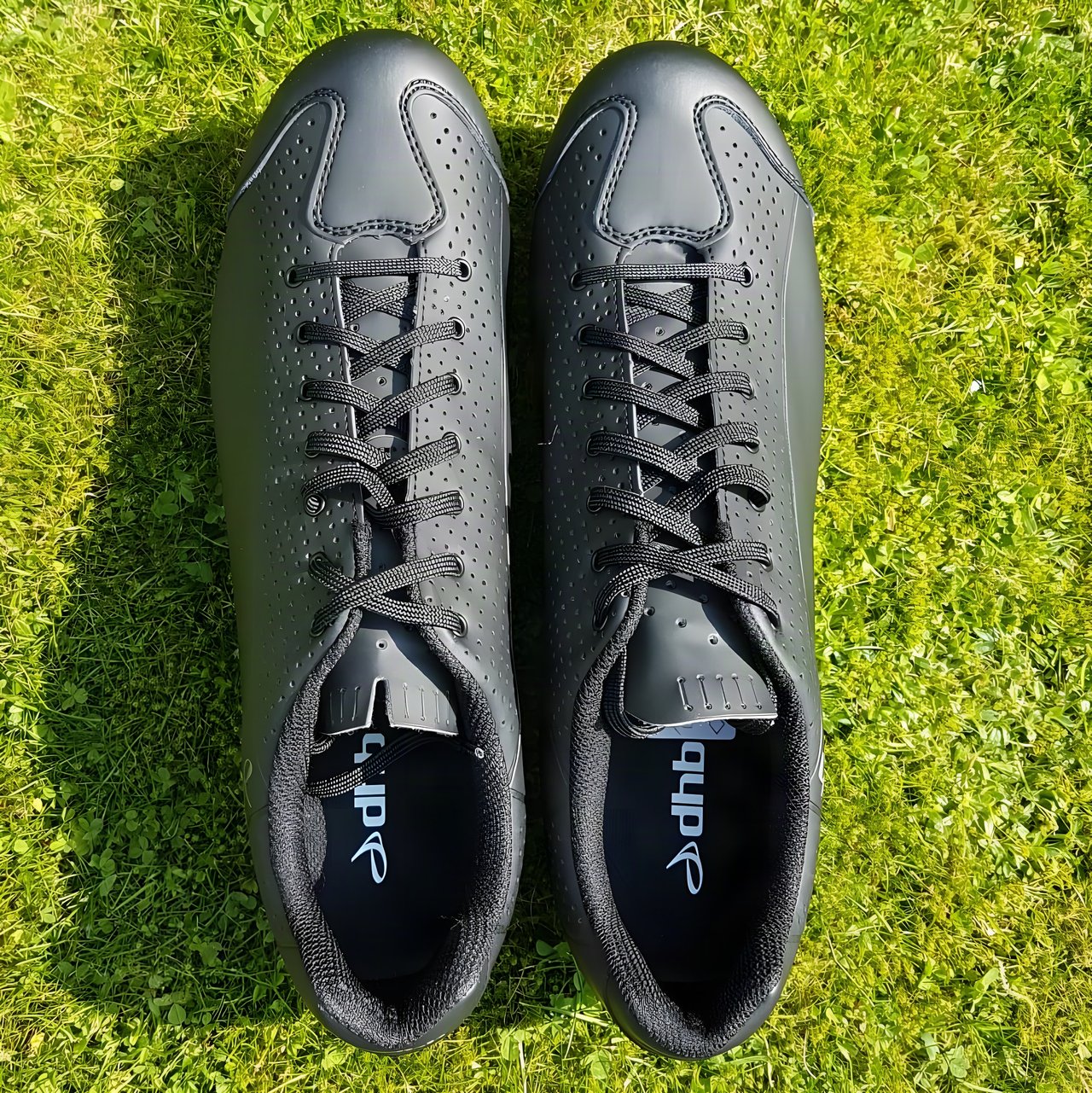 Pair of black dhb Dorica MTB lace-up shoes seen from above on a grass lawn.