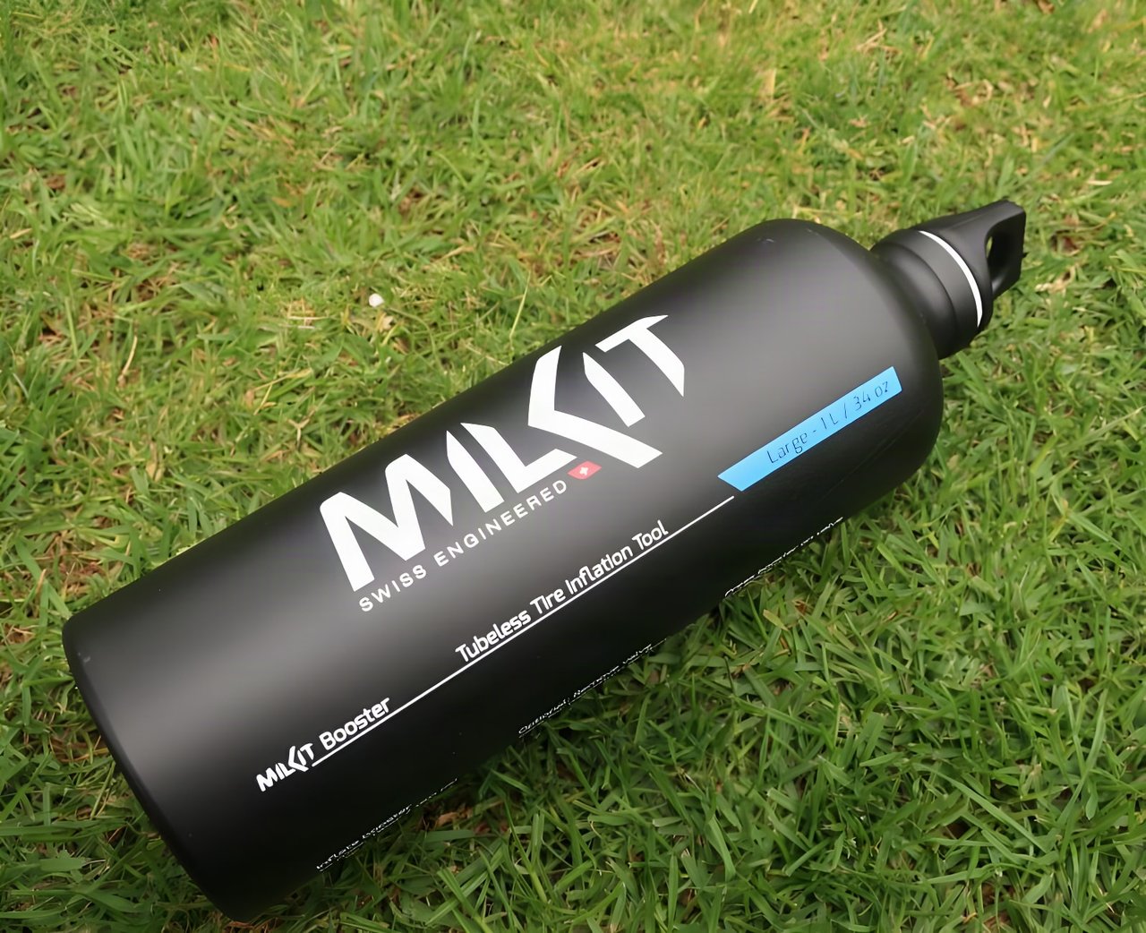 MilKit Booster tubeless inflator's black 1 litre aluminium bottle lying on grass.