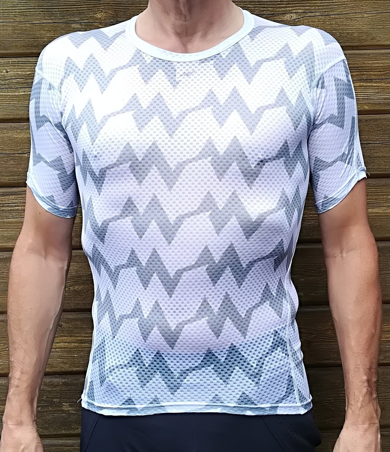 Morvelo Kuler short sleeve summer base layer in grey and white zigzag mesh, worn against a wooden fence.