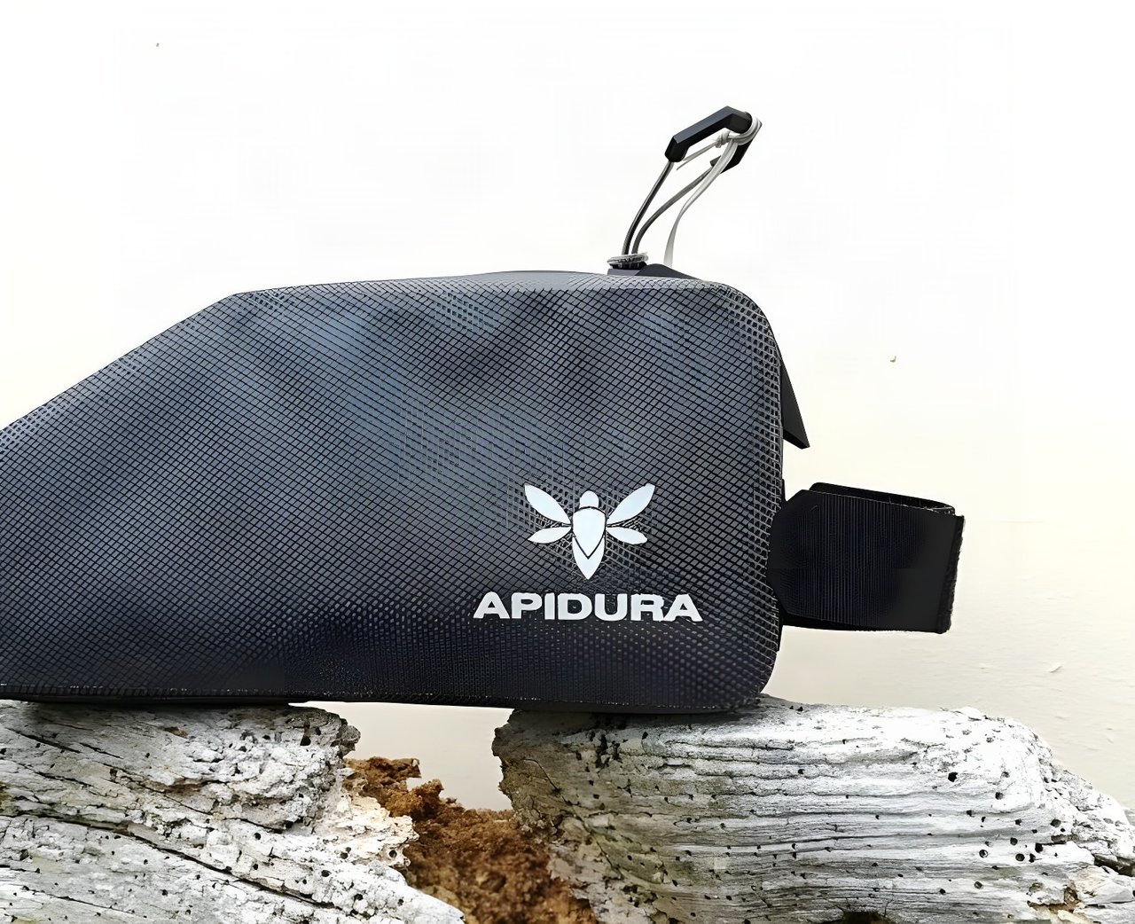 Apidura Expedition top tube bag in dark grey with silver logo, side view, resting on weathered wood.
