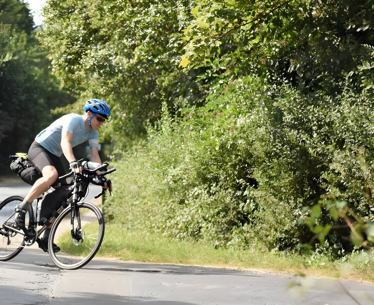 Rider on a loaded Kinesis GTD titanium ultra-endurance bike with frame and saddle bags on a leafy lane.