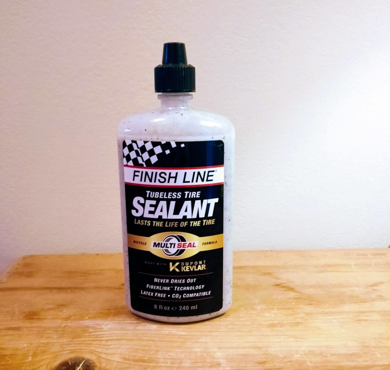 Bottle of Finish Line Tubeless Tyre Sealant, 240 ml, standing on a wooden table against a white wall.