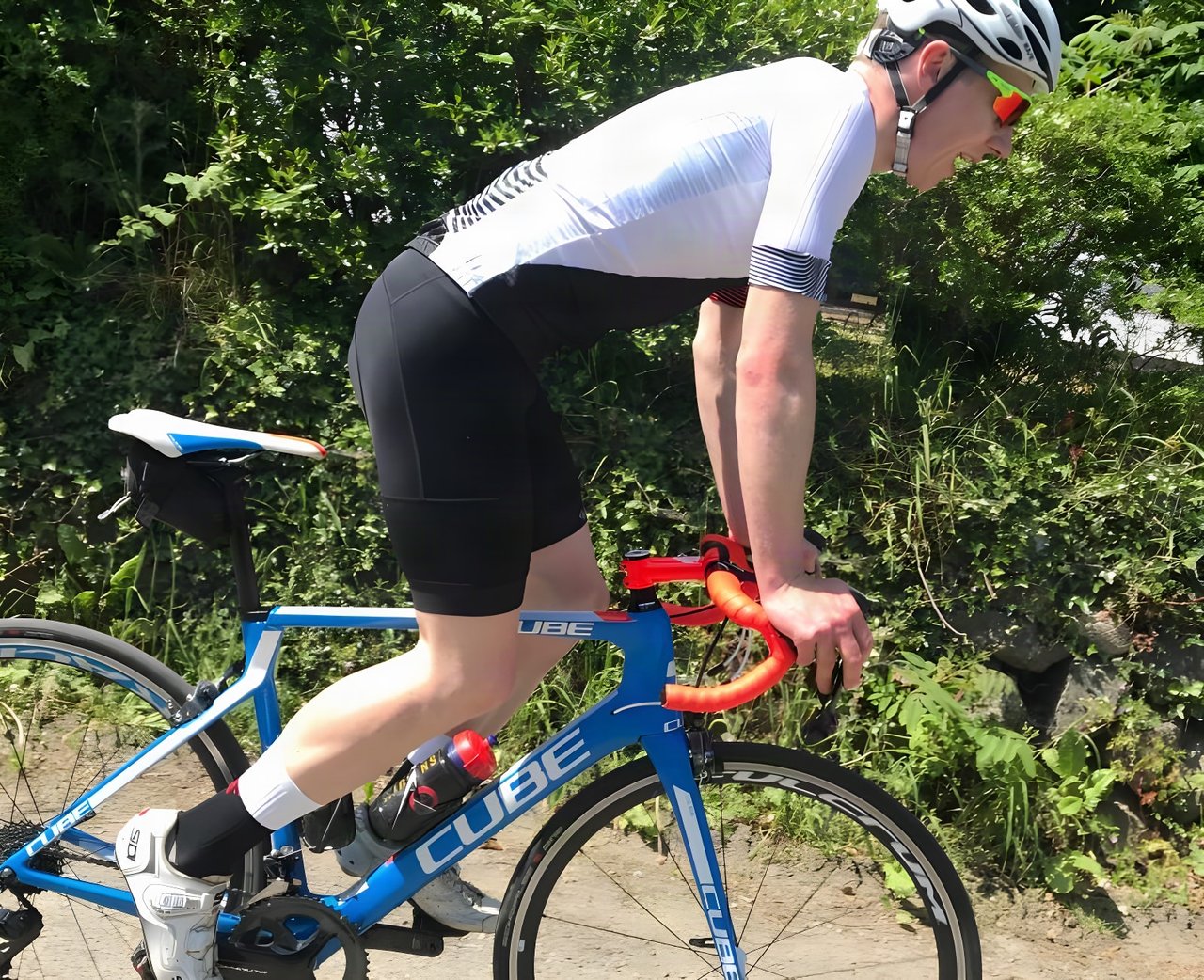 Rider in Galibier Peloton Lightweight bib shorts and a white jersey, riding a blue Cube road bike on a sunny lane.