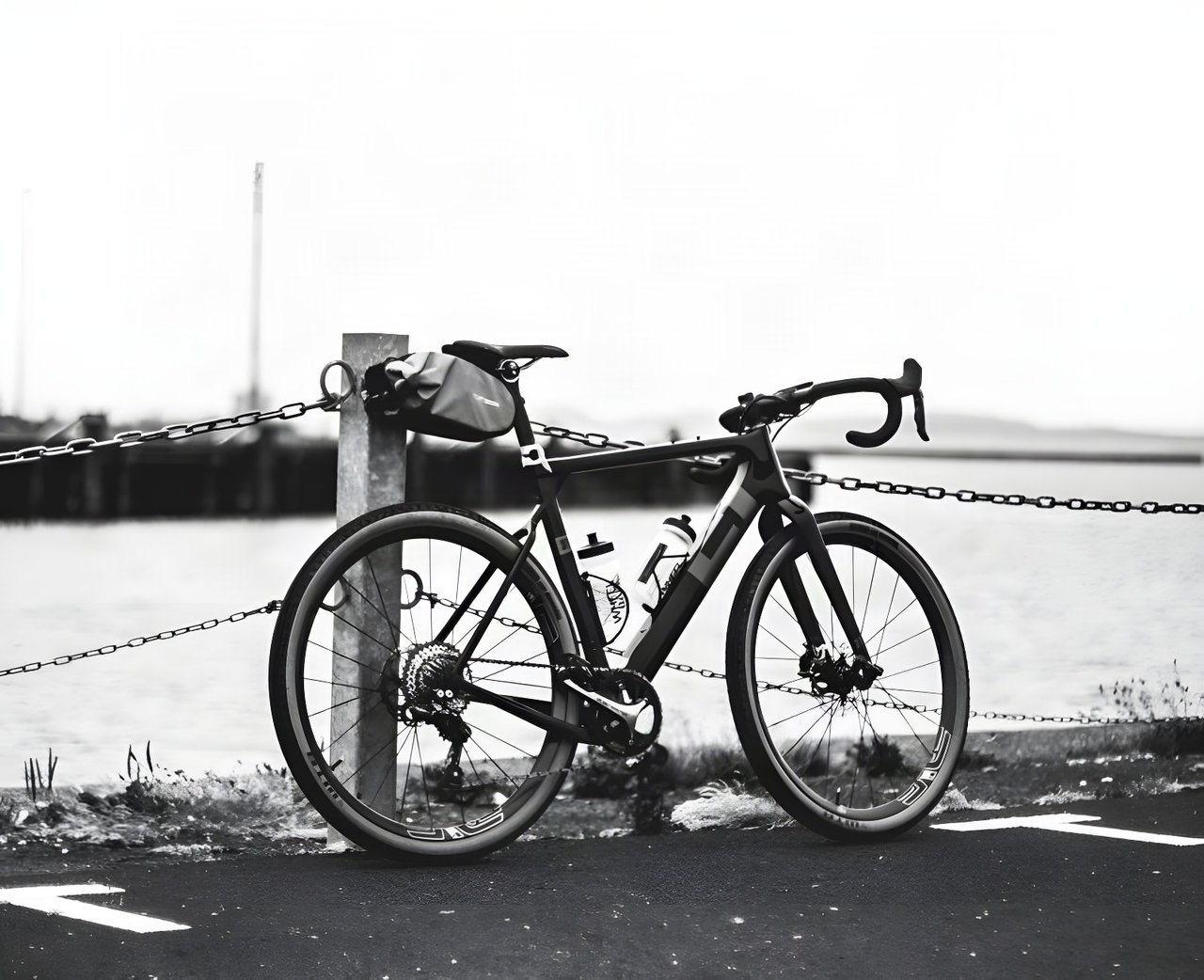 3T Exploro ridden at Grinduro Scotland, in black and white, with a saddle bag, leaning on a chained post by the docks.