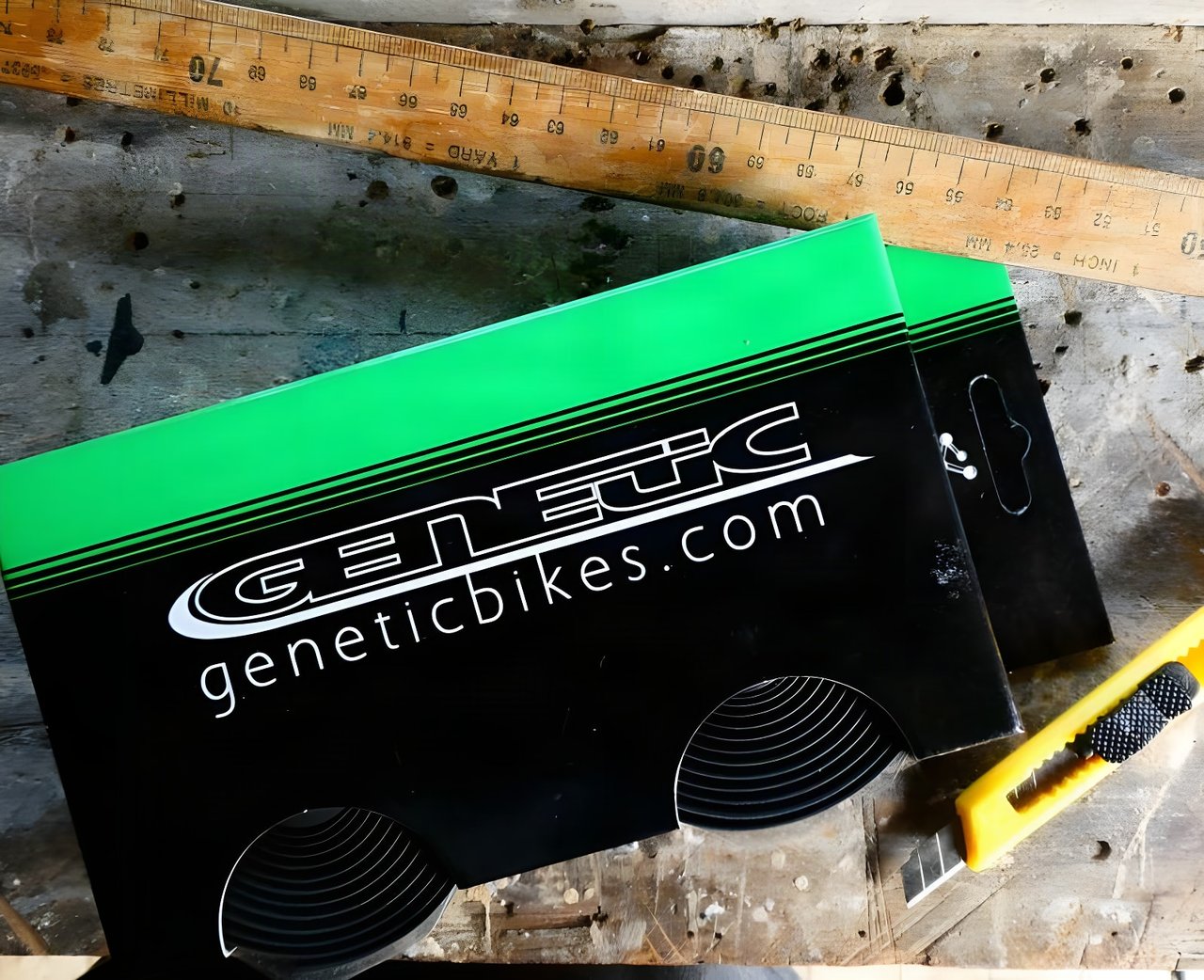 Two boxes of Genetic silicone bar tape on a workbench beside a wooden ruler and a yellow utility knife.