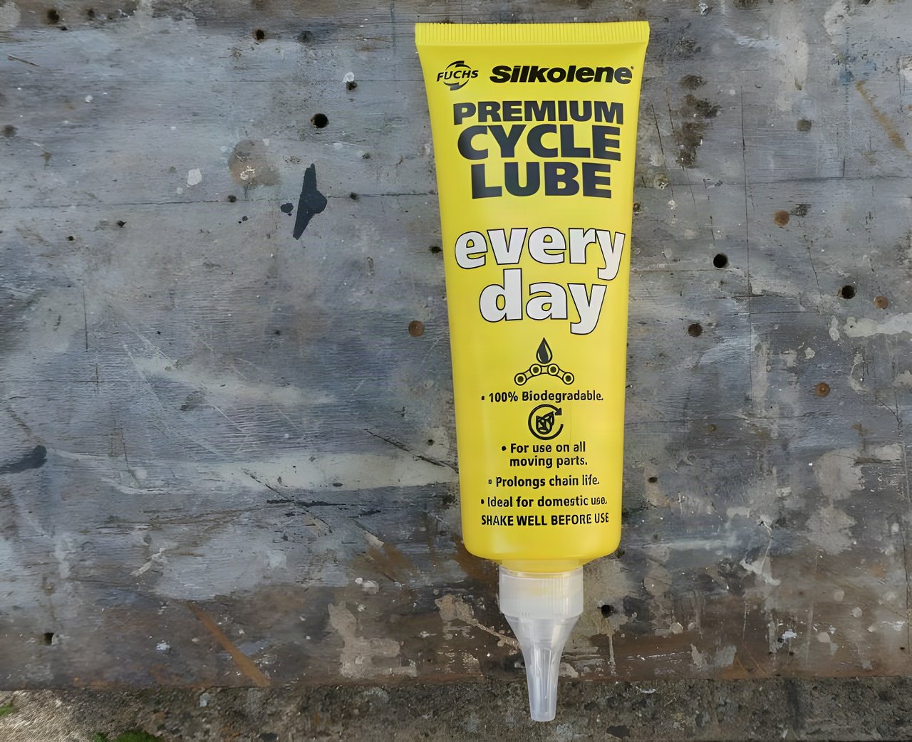 Yellow tube of Silkolene Premium Cycle Lube Every Day, a biodegradable chain lube, on a weathered workshop surface.
