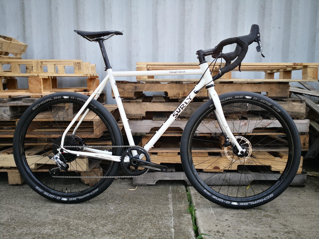 A white Surly Midnight Special leans against wooden pallets.