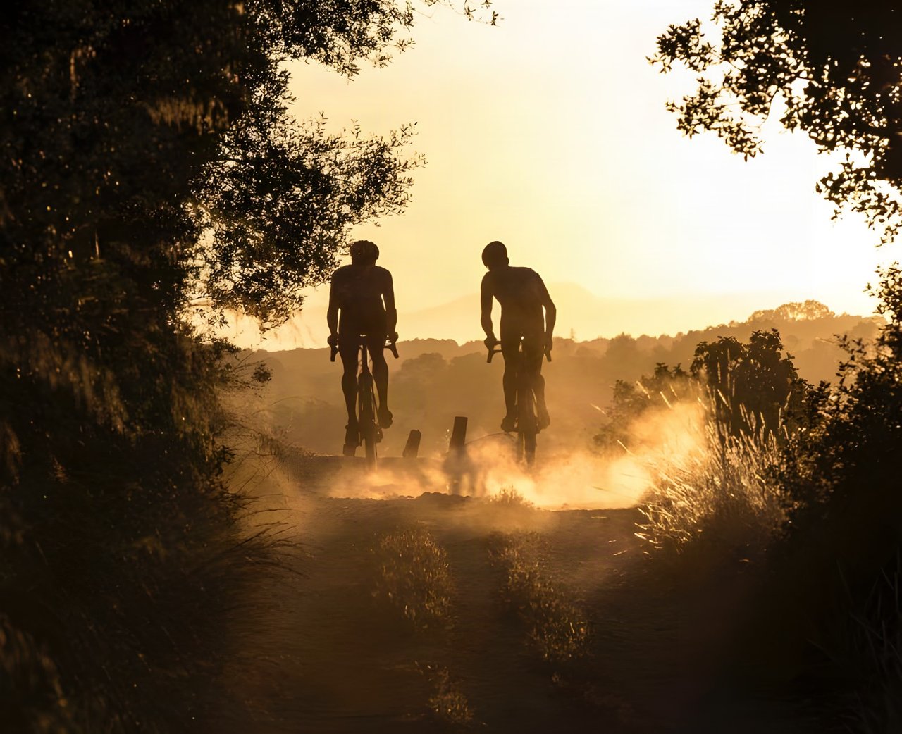 Two gravel riders silhouetted in dusty golden sunset light on a dirt track, promoting Toros de Gravel in Mallorca.