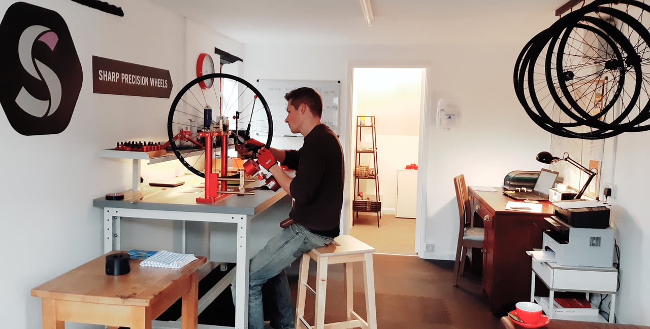 Ben Sharp trues a wheel on a red stand in his Sharp Precision Wheels workshop.
