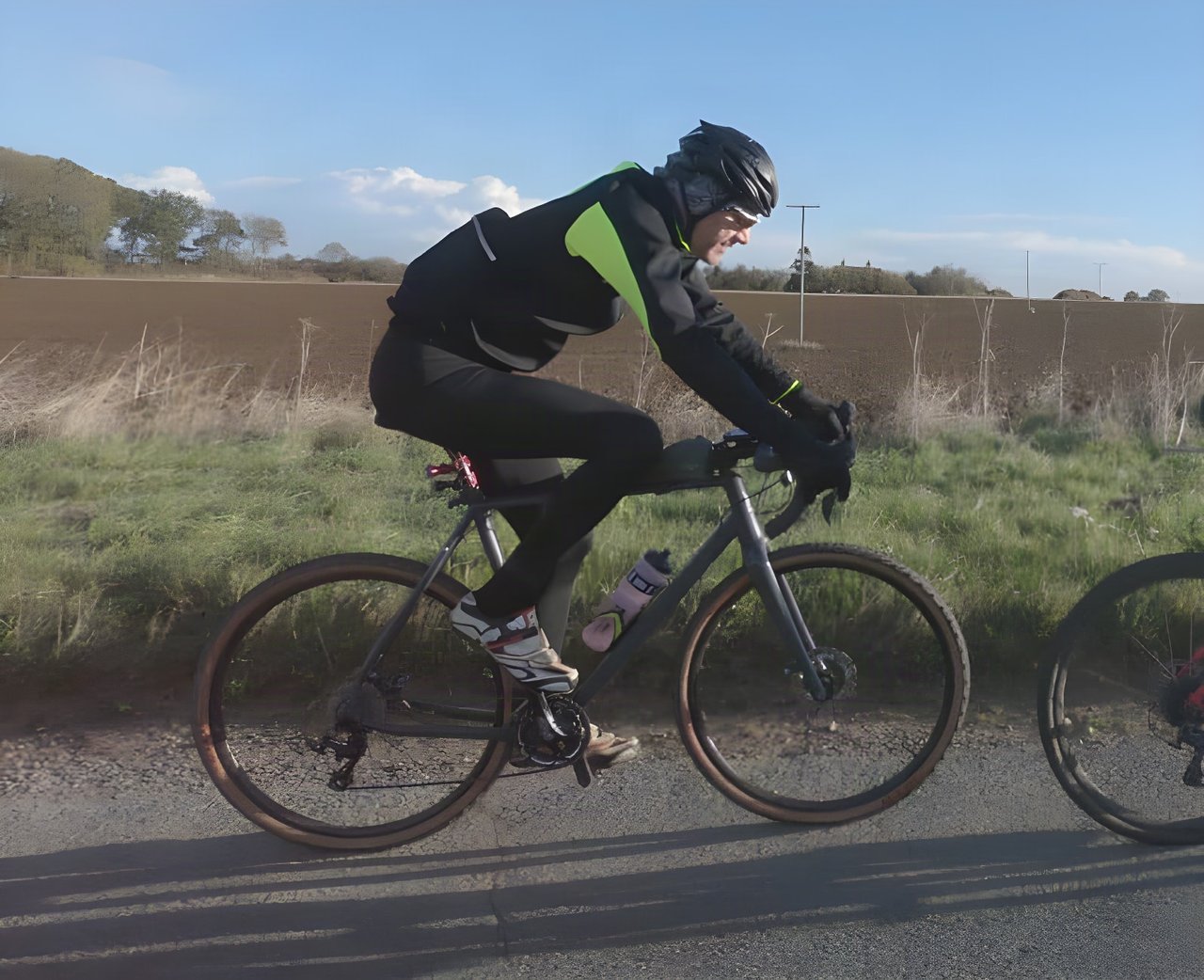 Rider in the black and hi-vis yellow Galibier Mistral Foul Weather Jacket on a gravel bike beside a Suffolk field.
