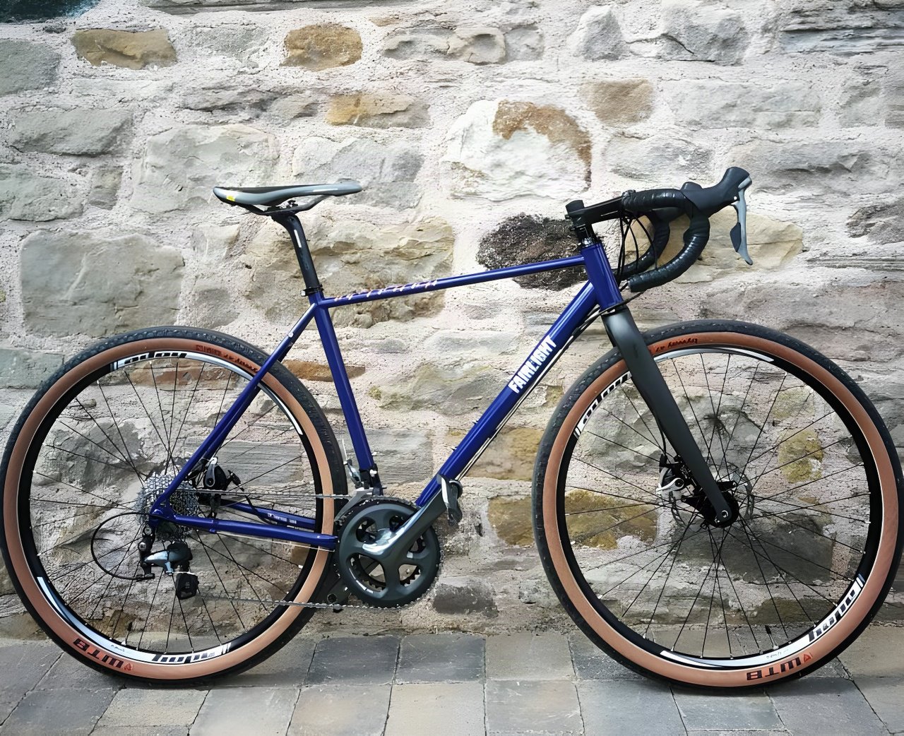 Mark Downie's blue Fairlight Secan gravel bike with tan-wall WTB tyres against a stone wall.