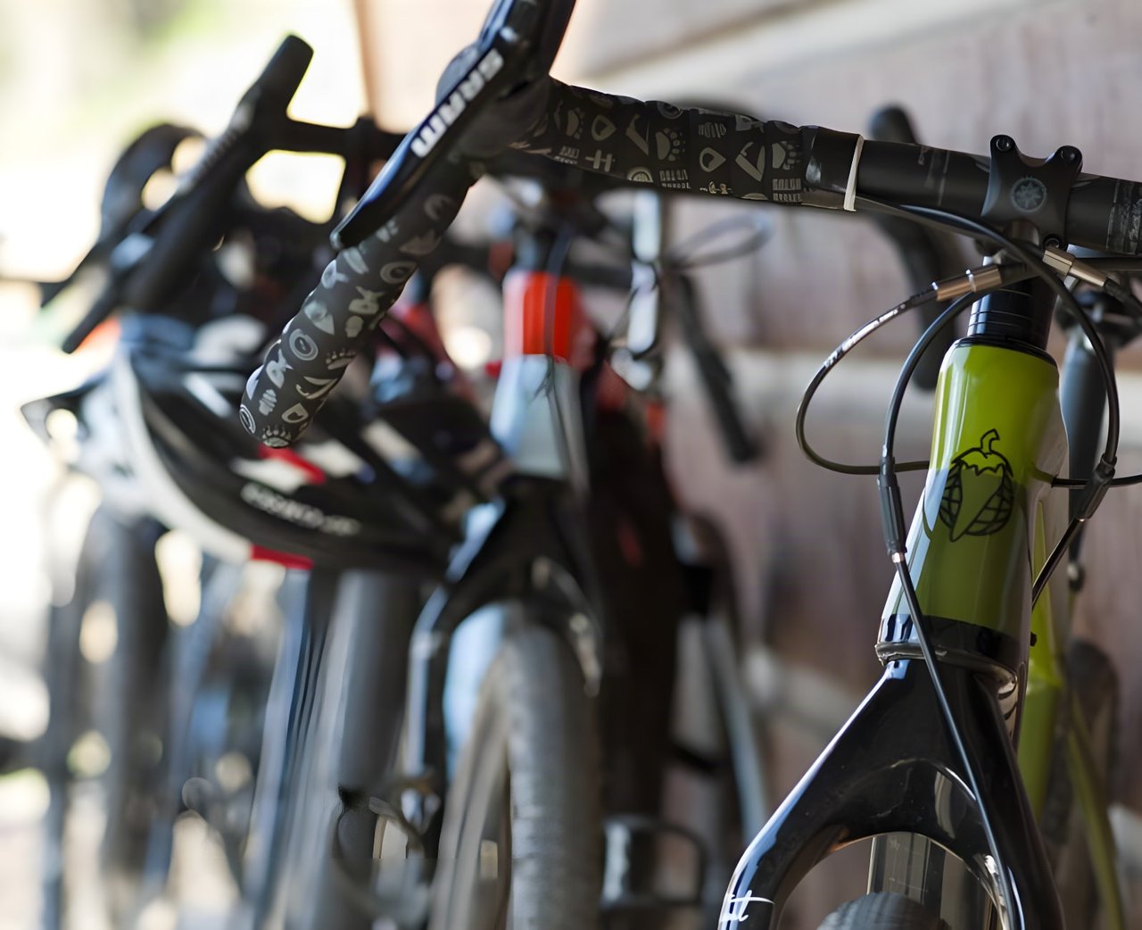 Green Salsa gravel bike with SRAM drop bars and patterned bar tape, other bikes blurred behind it.