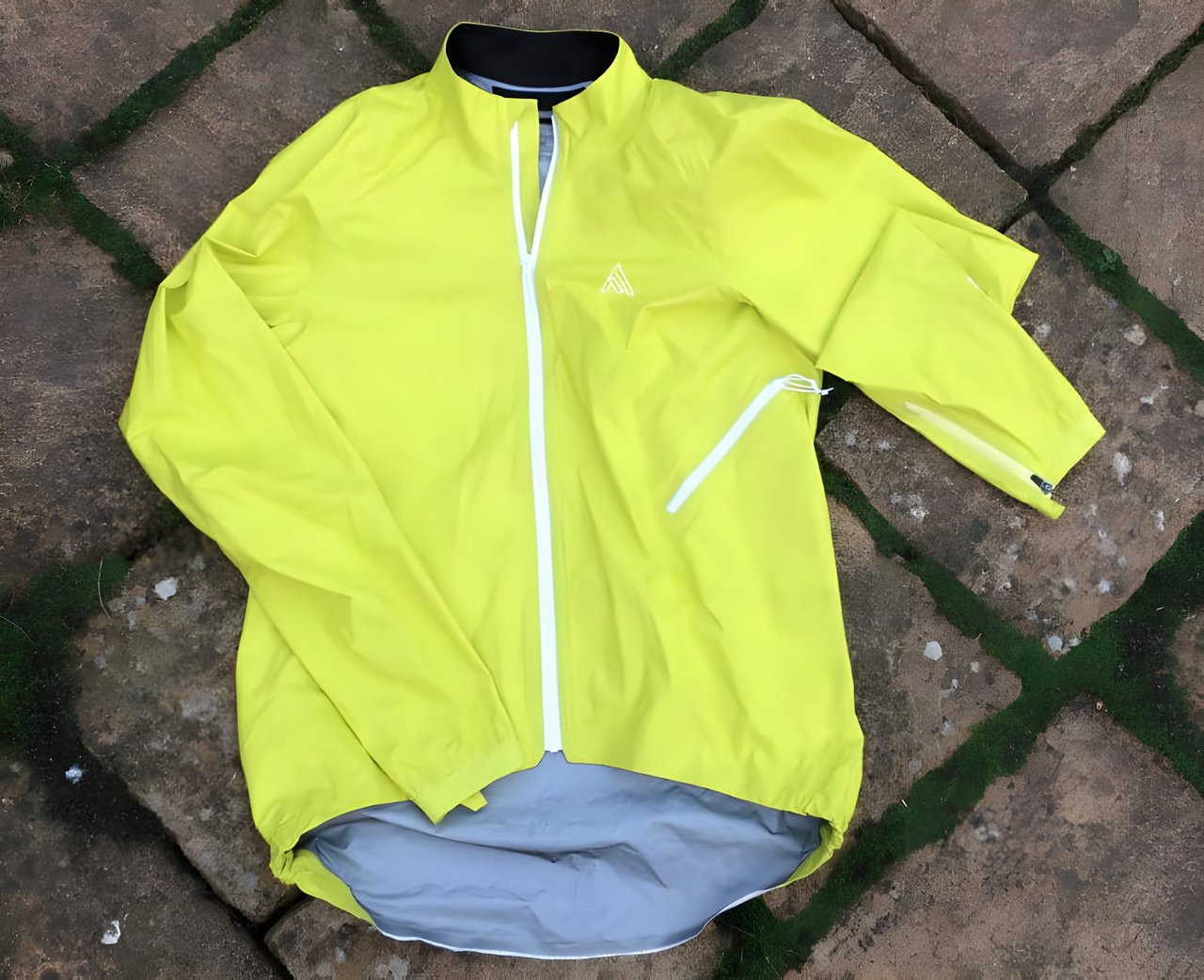 Rider in a neon yellow 7Mesh Rebellion waterproof jacket and white helmet, standing in front of a gravel bike.