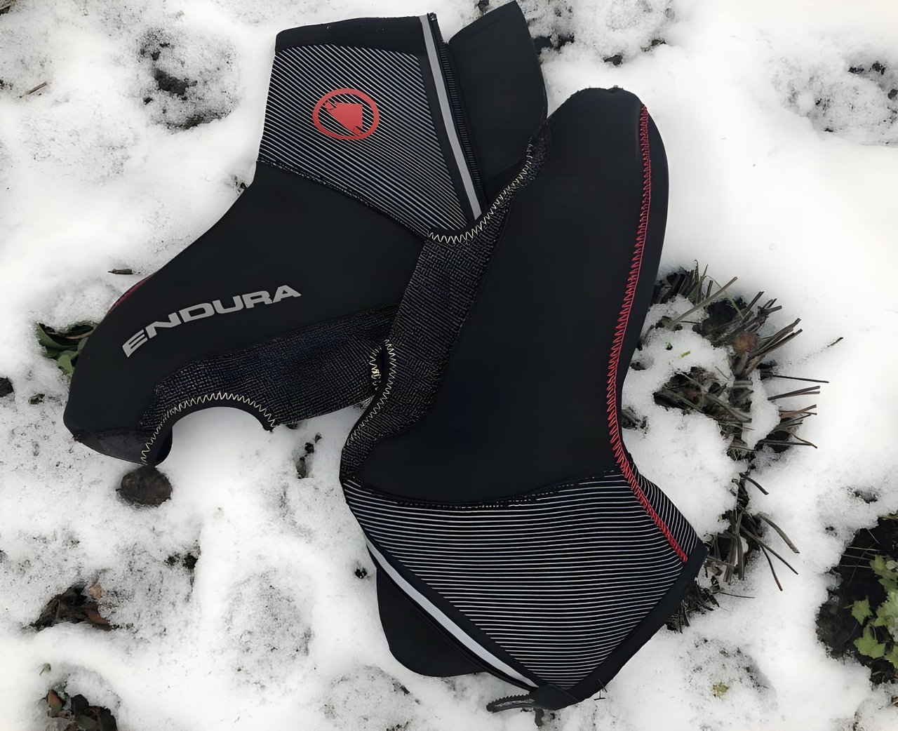 Pair of black Endura Freezing Point overshoes with red logo and reflective trim lying on snow.