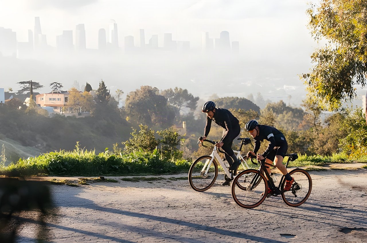 Two riders on Salsa Warroad road bikes ride a hillside road above a hazy city skyline.