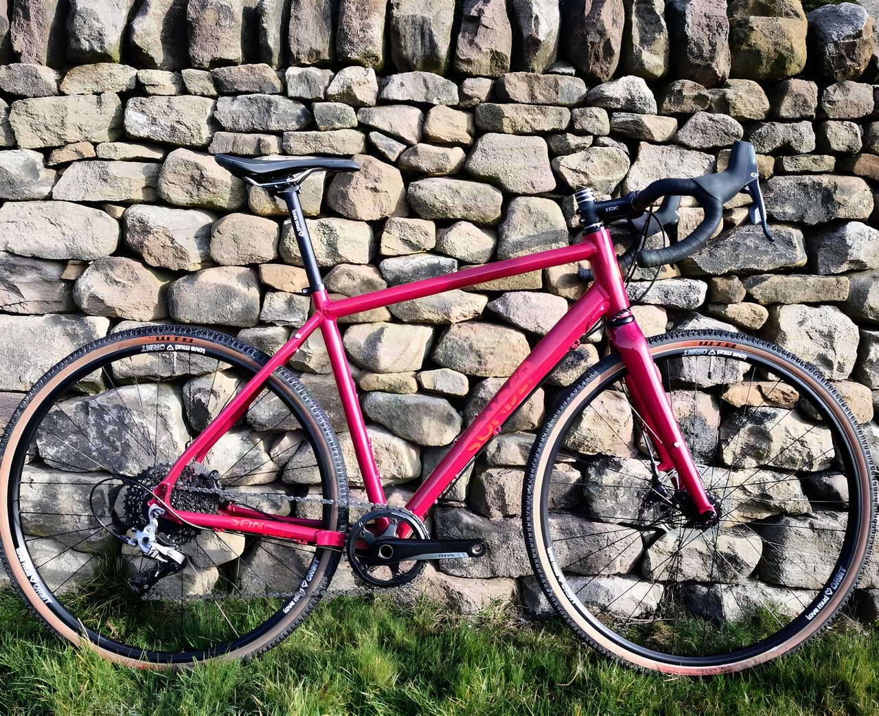 Red Sonder Camino AL gravel bike with SRAM Rival 1 and tan-wall tyres, leaning against a dry-stone wall.