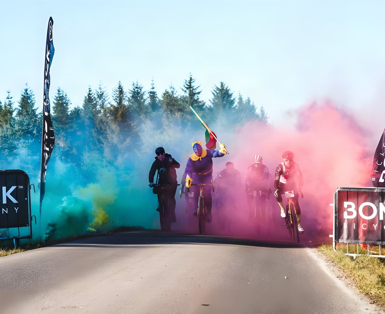 Dirty Reiver 2019 riders emerge from coloured smoke at the start in Kielder Forest, past Bombtrack banners.