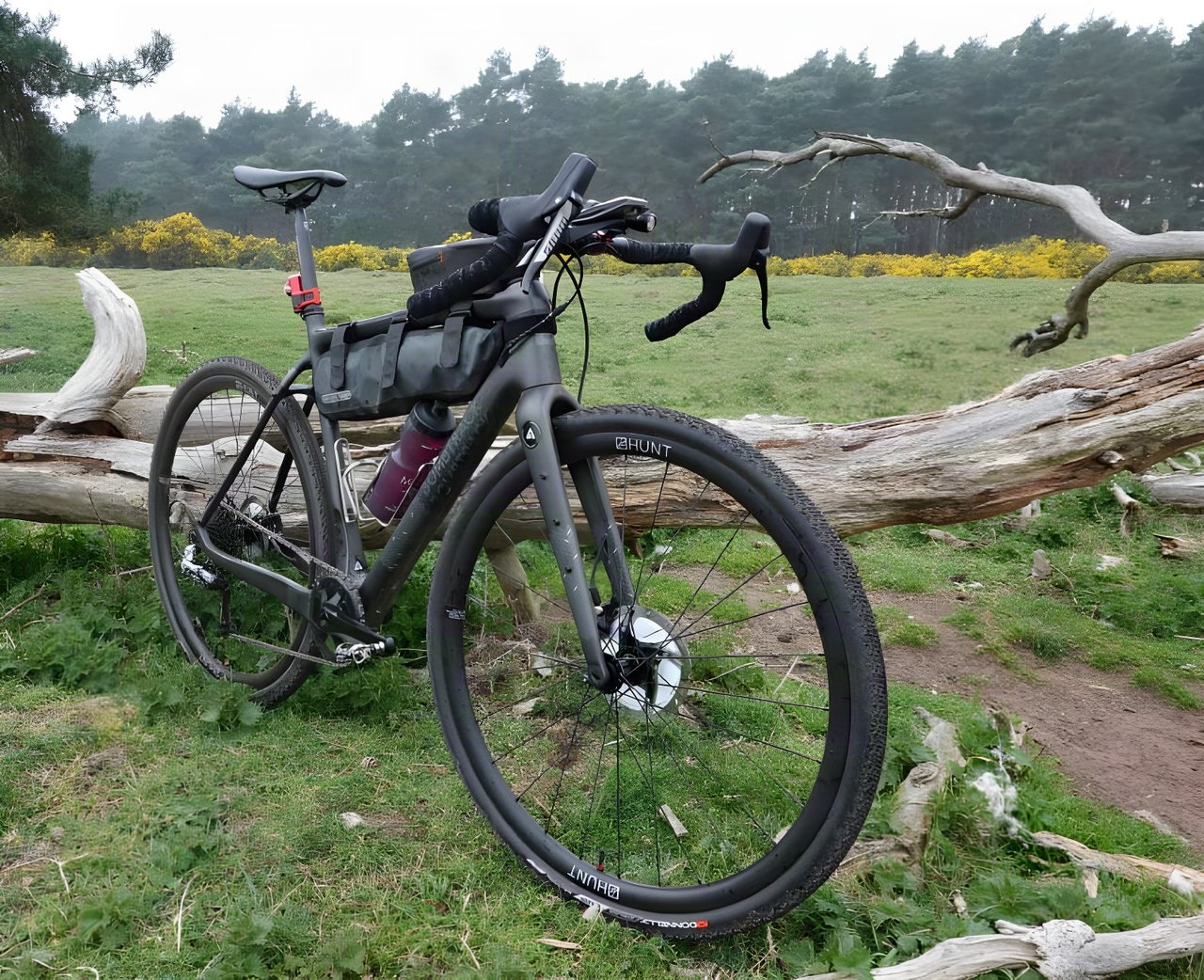 Bombtrack Hook EXT-C gravel bike with an Ortlieb frame bag, set up for the Dirty Reiver, beside a fallen tree.