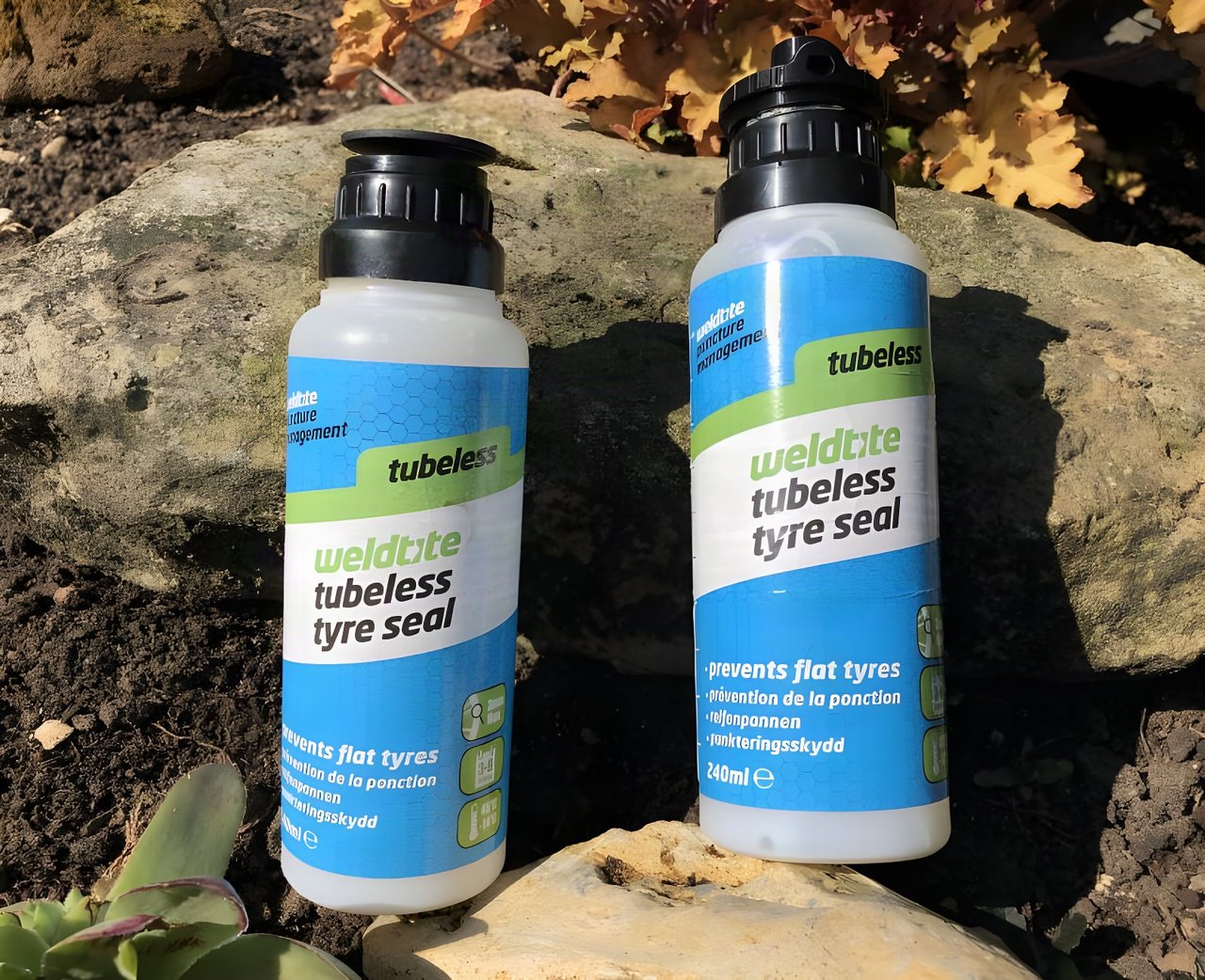 Two 240ml bottles of Weldtite Tubeless Tyre Seal standing against a garden rock in sunshine.