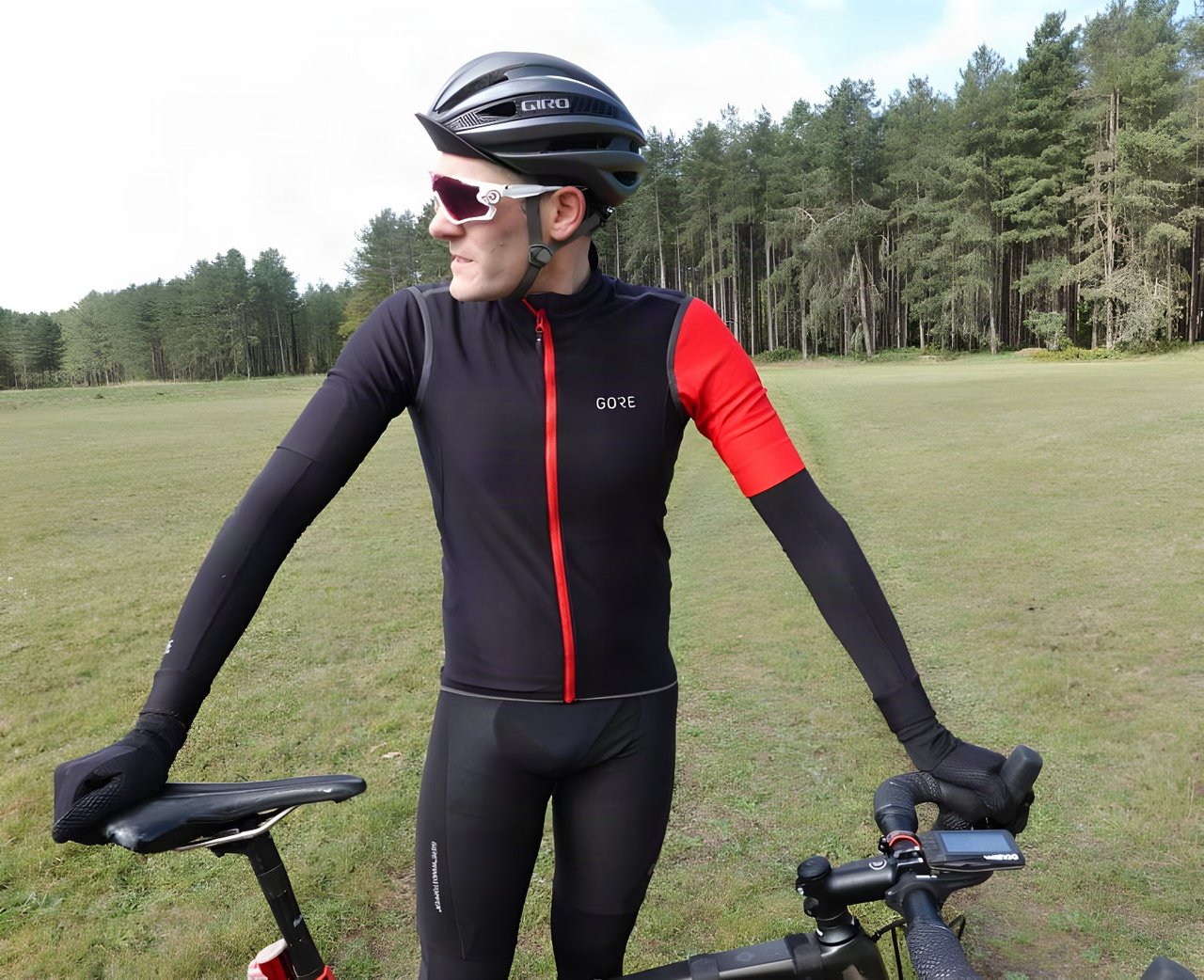 Rider in a black Gore C5 Gore-Tex Infinium softshell jersey with red zip and sleeve, standing by a gravel bike.