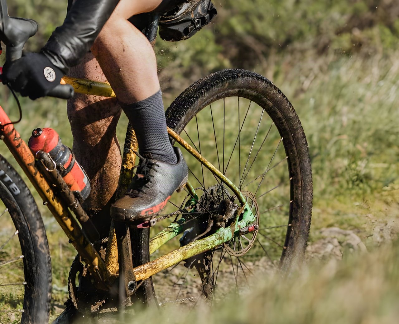 Rider's muddy leg and shoe on a gravel bike, pedalling over rough ground on WTB Venture 700c tyres.