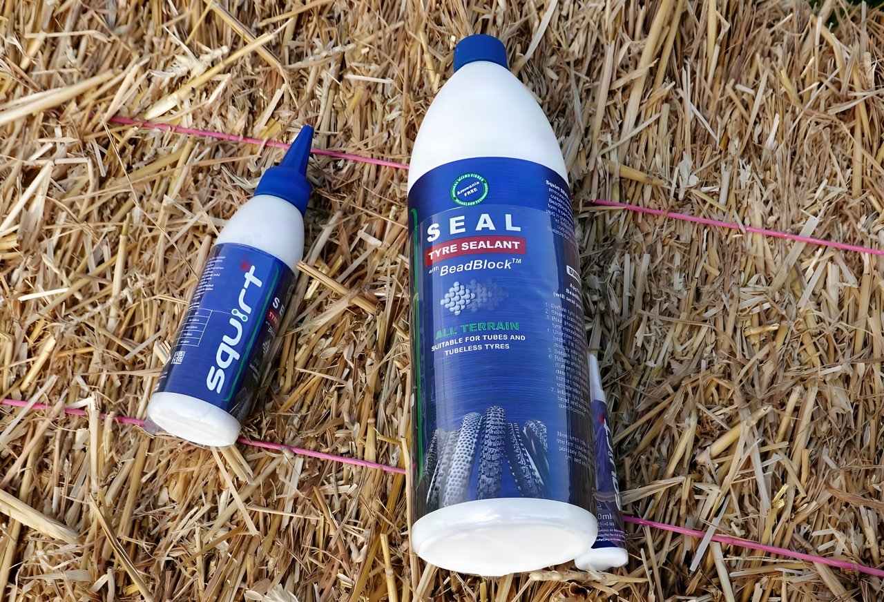Squirt Seal tyre sealant with BeadBlock in 1 litre and 150ml bottles lying on a straw bale.