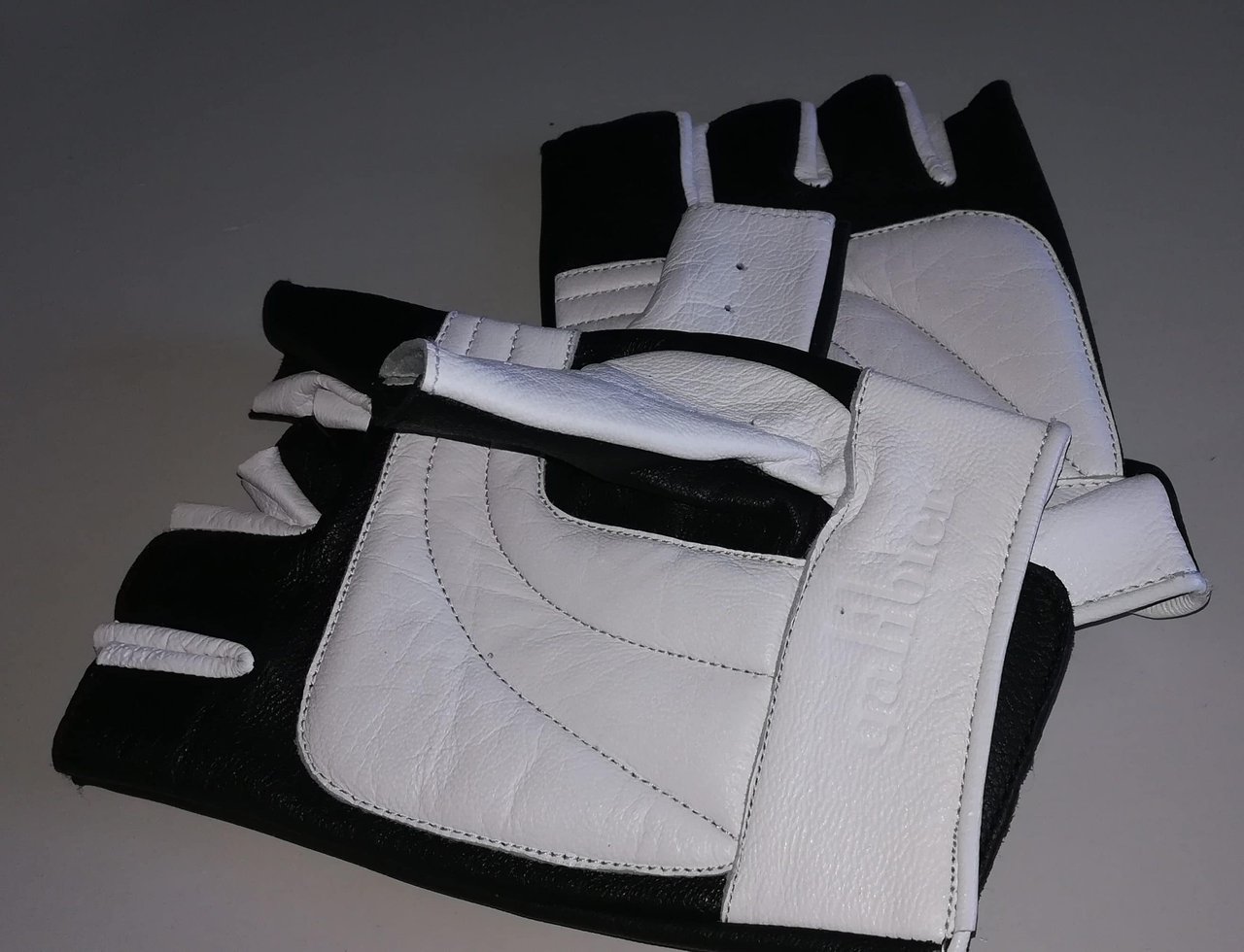 A pair of white and black leather Galibier Ginettaccio track mitts laid on a table.
