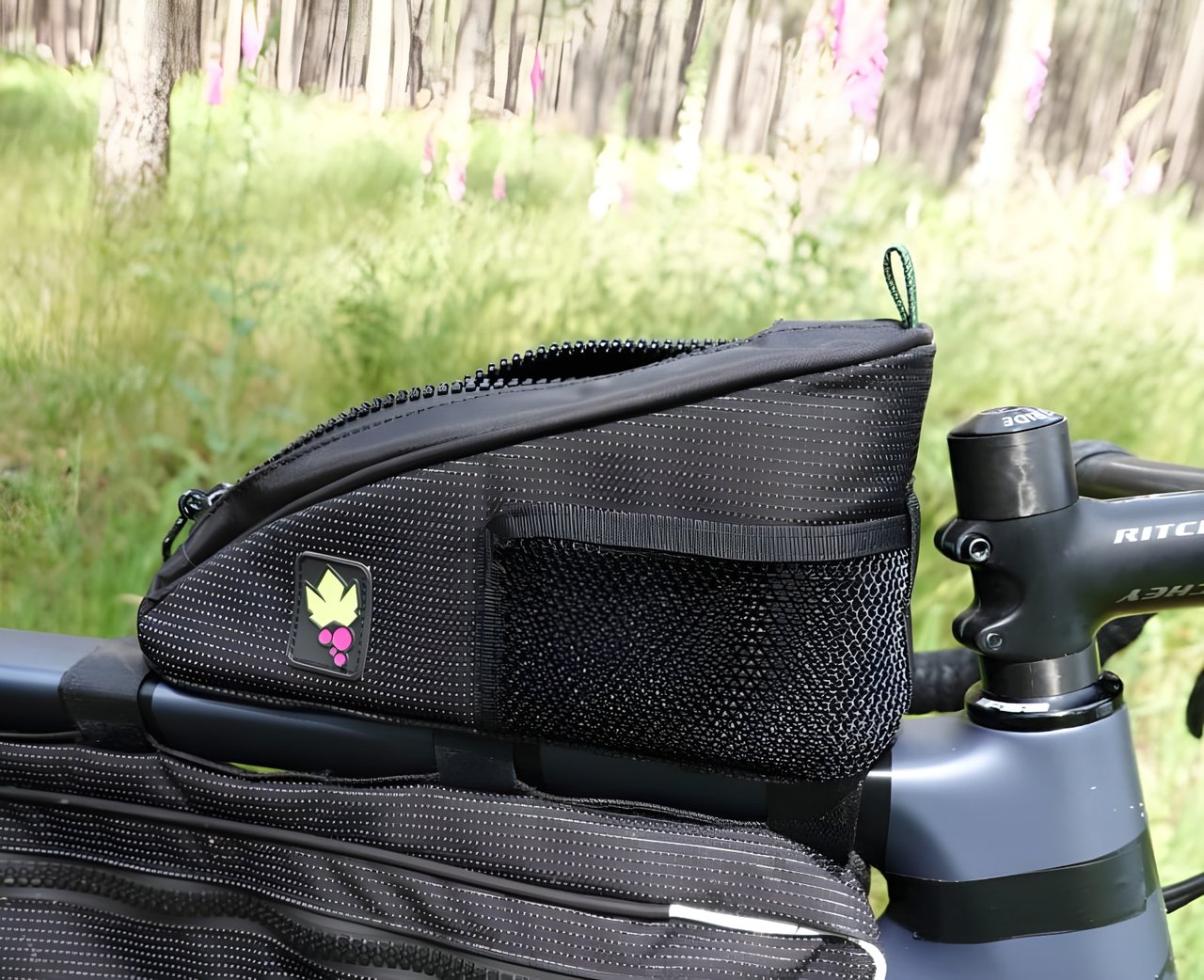Miss Grape Node 2H top tube bag with its mesh side pocket and full-length zip, on a bike in front of woodland.